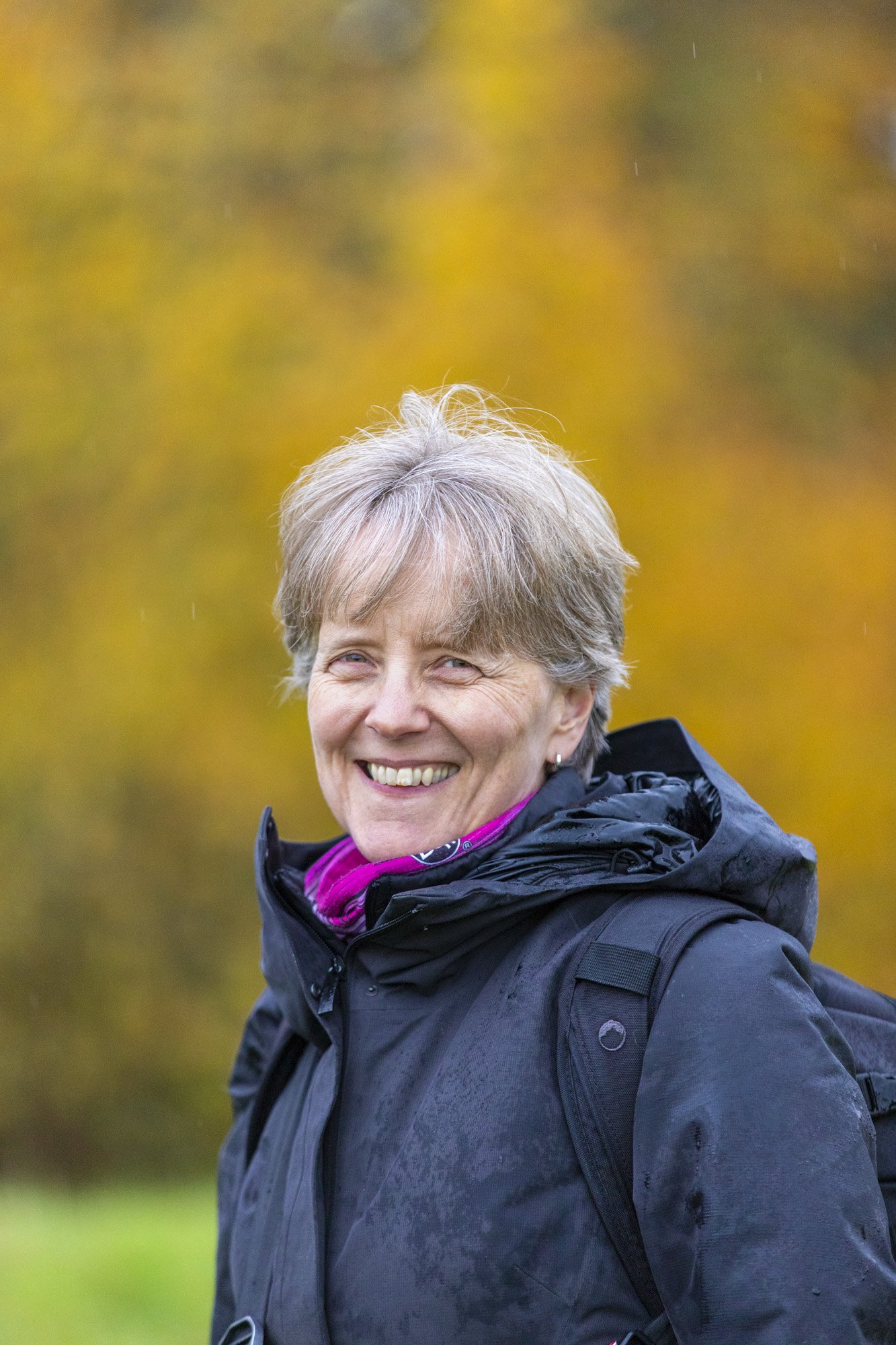 Professional pet photographer Laura Galbraith is pictured smiling looking towards the camera on an overcast autumn day with beautifully blurred orange tones in the background.