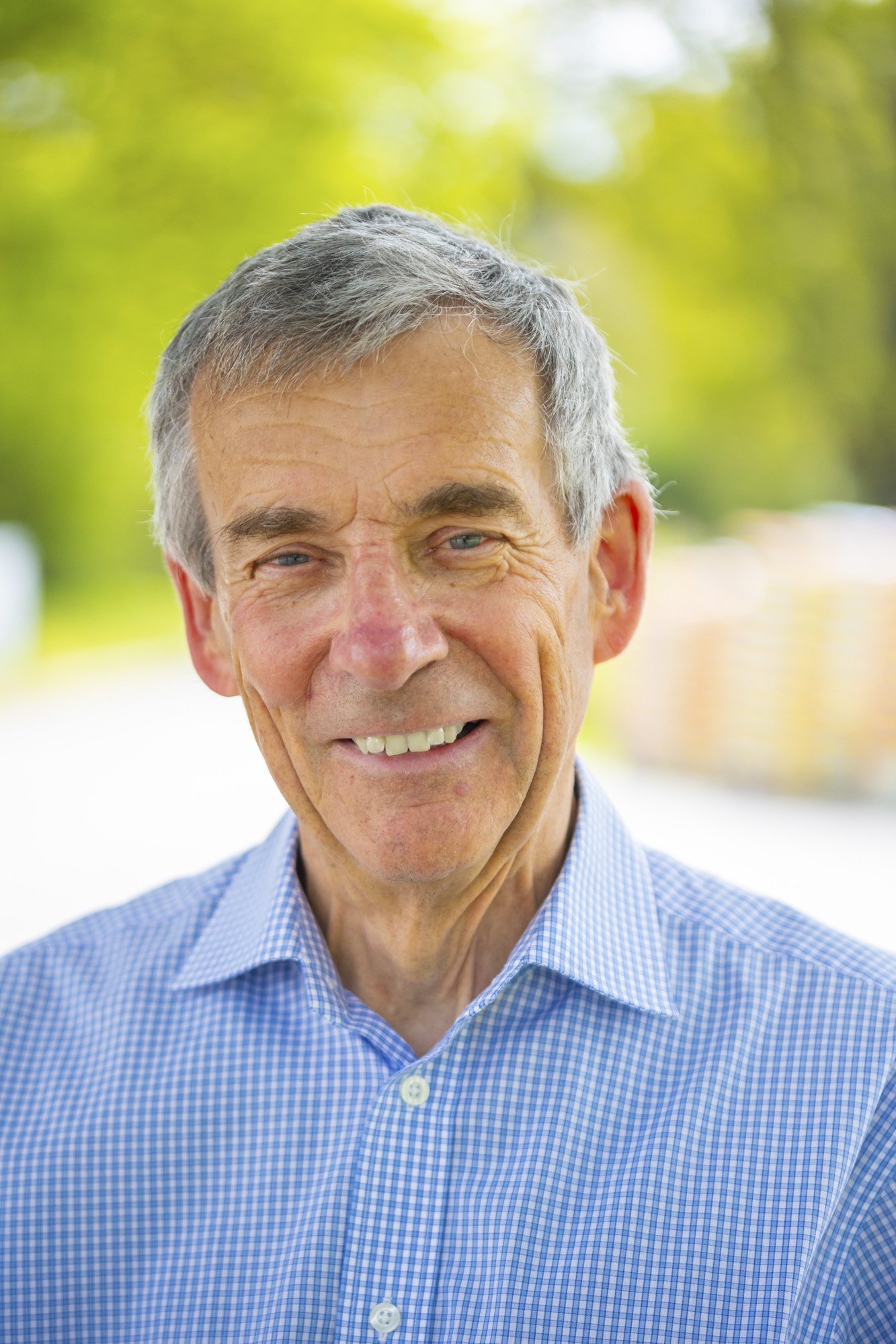 A man poses for a headshot outdoors on a beautiful sunny day.
