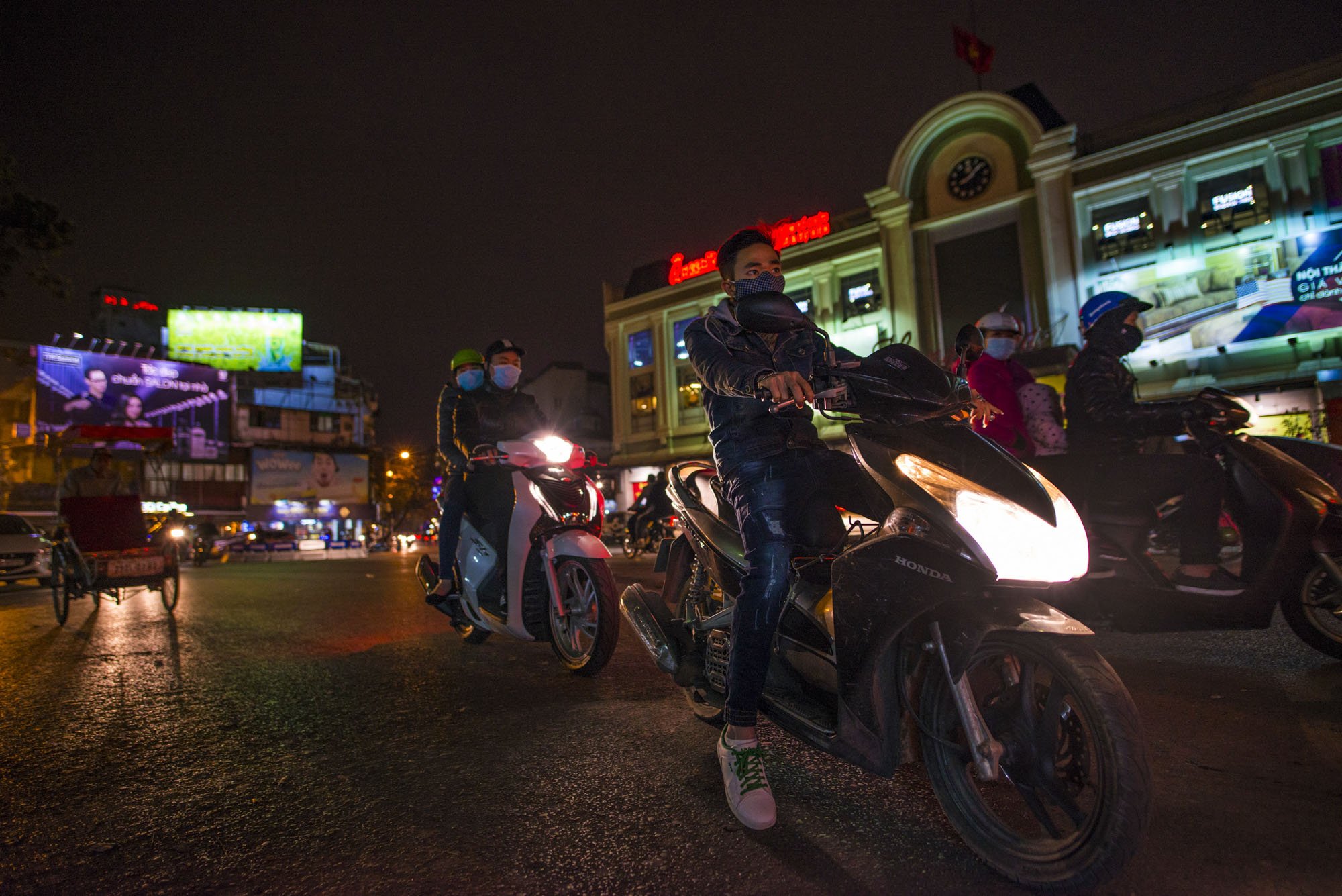 A night shot taken in Hanoi, Vietnam. It's taken at night and low angle showing several scooter riders on motorbikes.