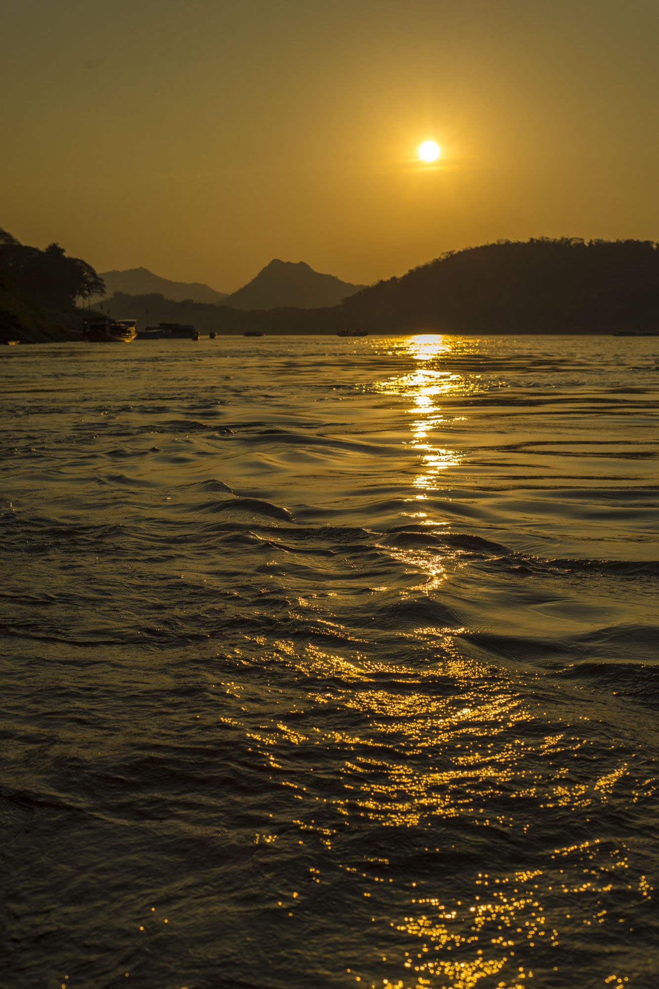 A picturesque sunset over Luang Prabang in Laos. This image shows the sun setting in the distance over the Mekong river with the sun light reflected beautifully in the ripples of the water. It's a tranquil scene with no boats in the river making it v