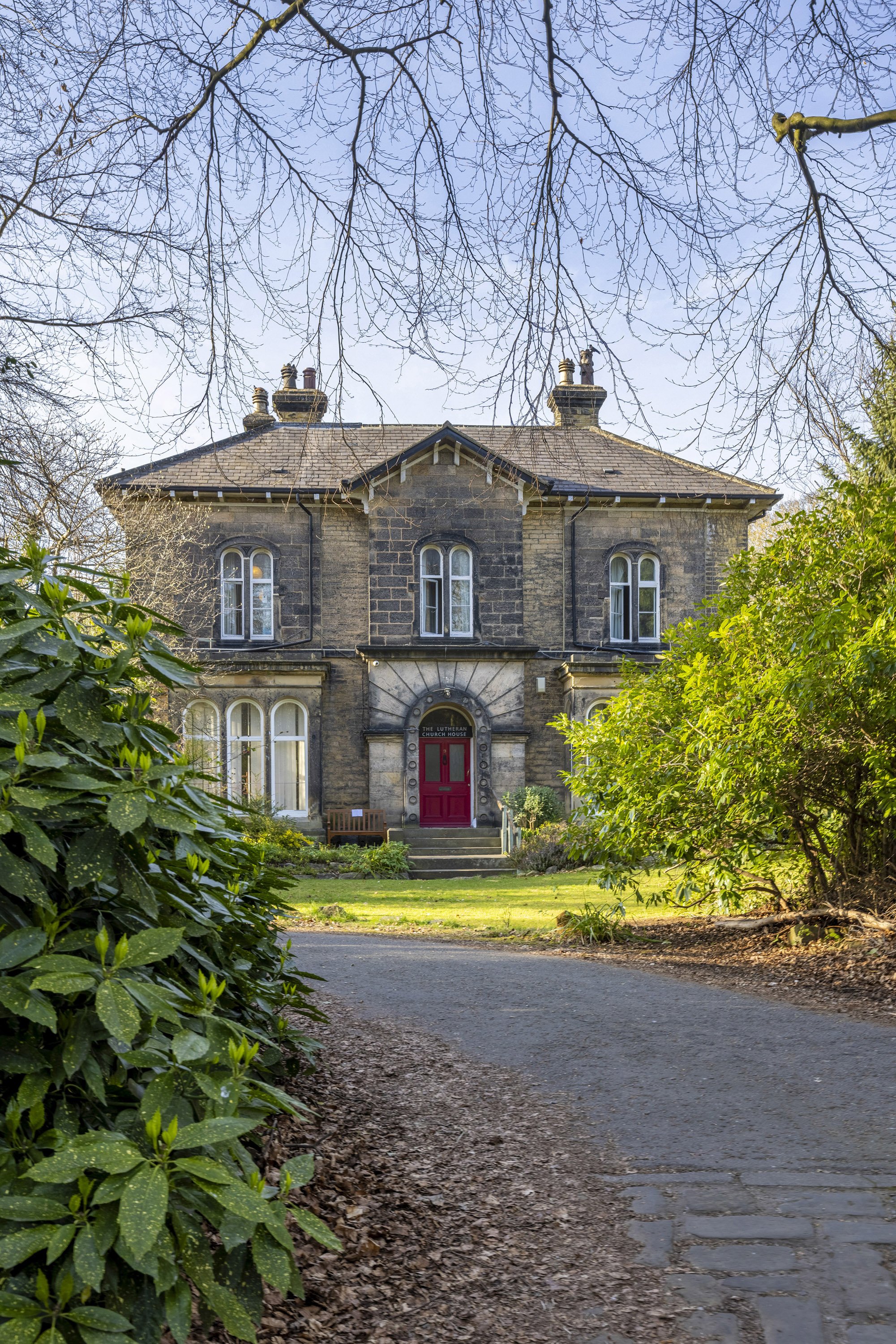 The entrance of a building with a red door is photographed from its driveway.