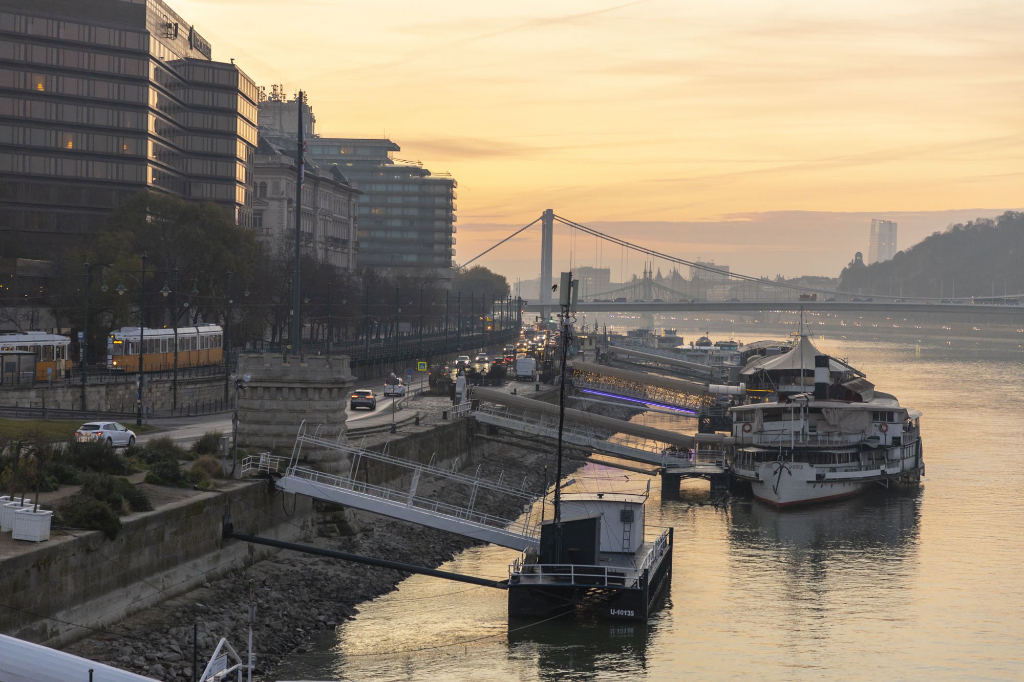A sunrise photo over Budapest, Hungary with boats in the Danube river with sunrise tones behind.