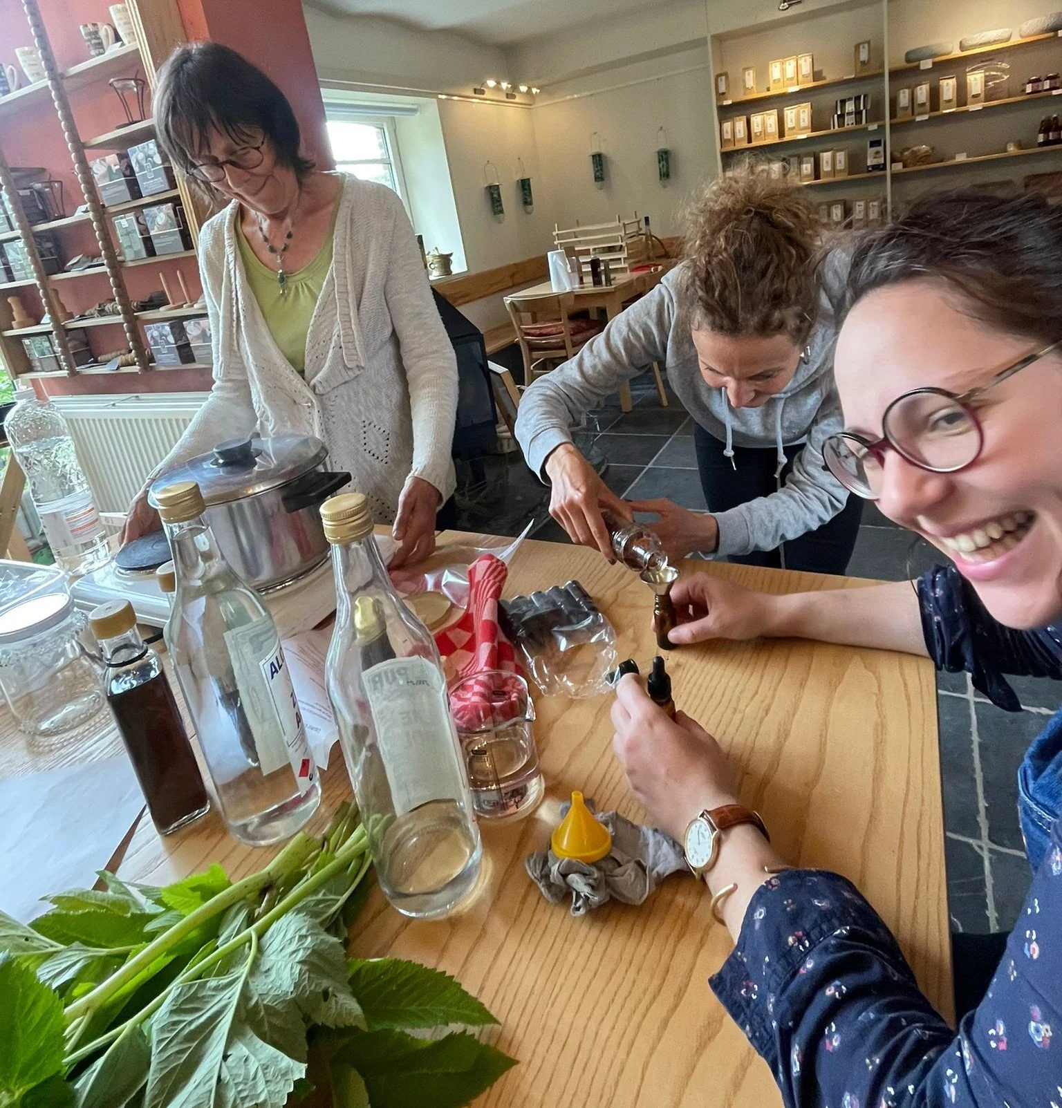 Trois femmes rigolant et préparant des ingrédients dans un atelier d'herboristerie.
