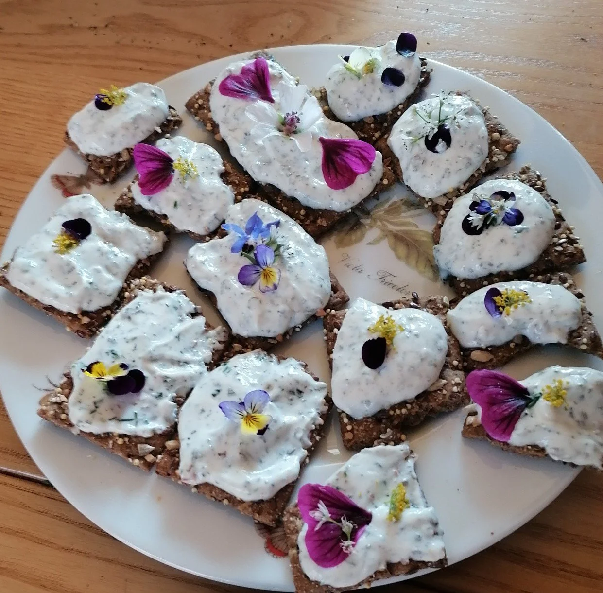 Tranches de pain complet avec une garniture de fromage blanc aux herbes du jardin, décorées de fleurs comestibles colorées.
