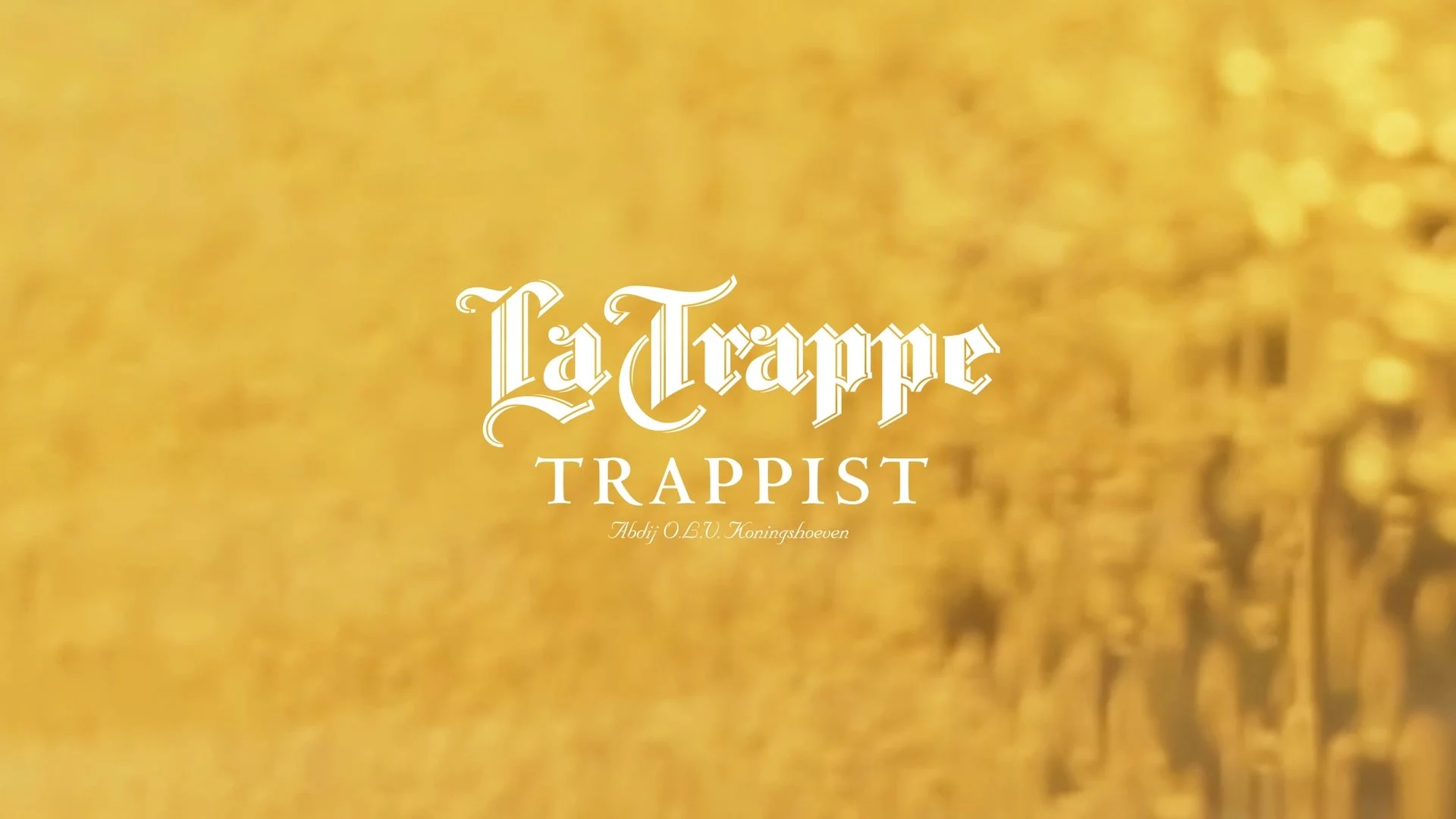 Title screen with the text 'La Trappe TRAPPIST Abdij O.L.V. Koningshoeven' over a gold-colored background with blurred detailing.