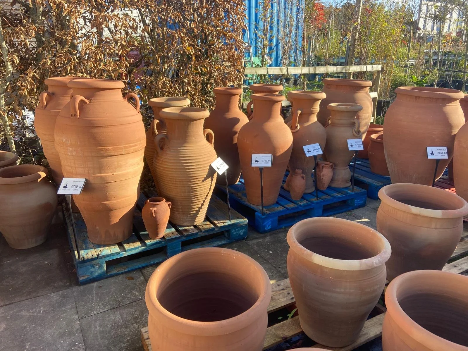 A range of Nile Terracotta pots and vases displayed on pallets at an outdoor market. Price tags are visible on some items.