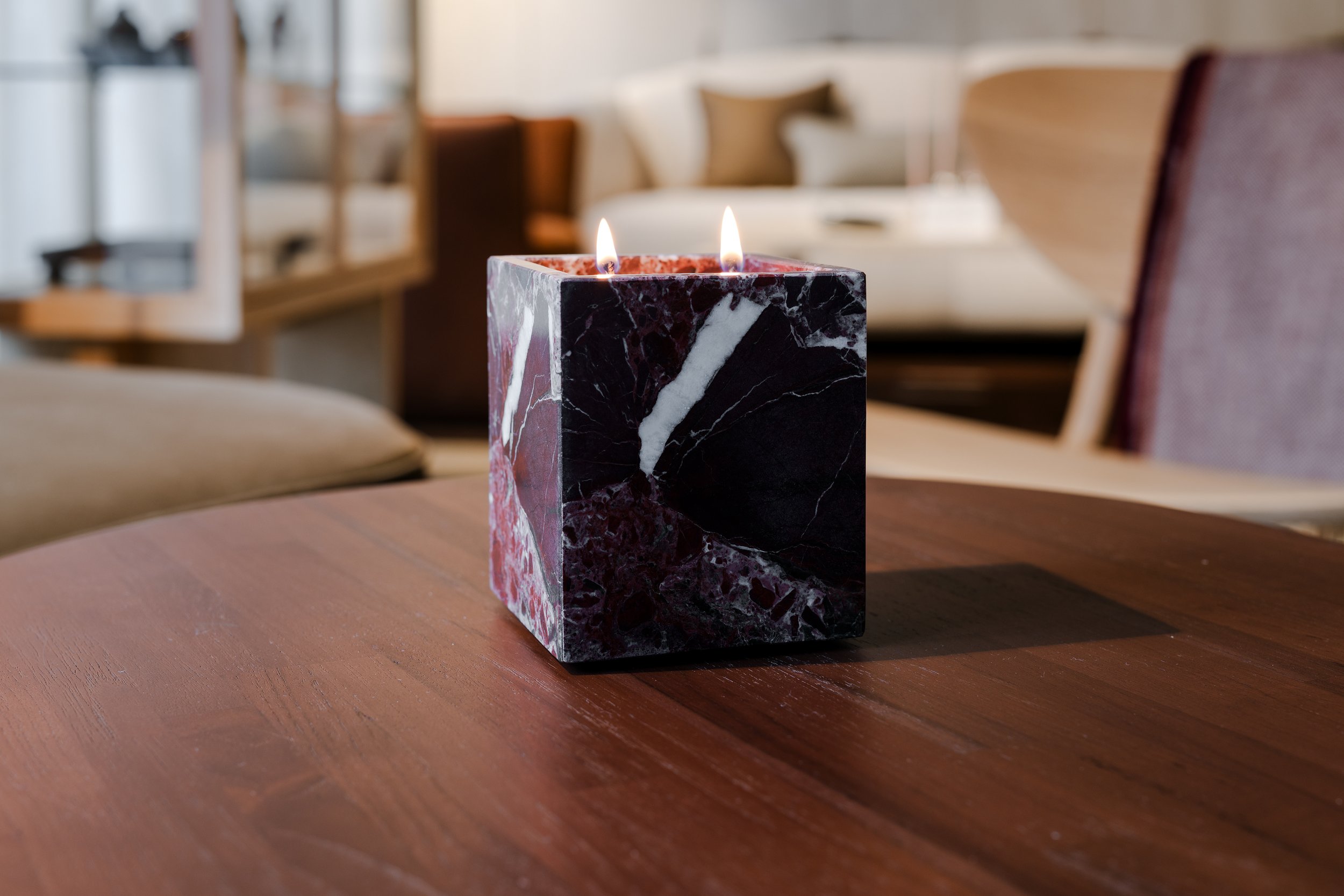A marble candle holder with two lit candles on a wooden table in a cozy living room.
