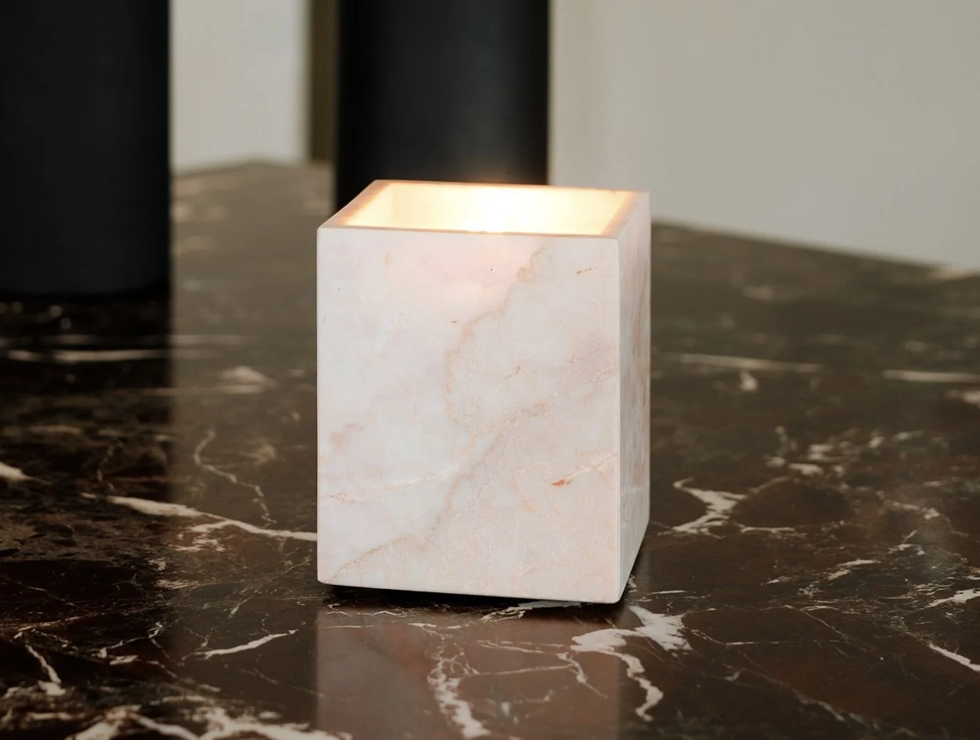 A lit square-shaped marble candle holder on a dark marble surface.