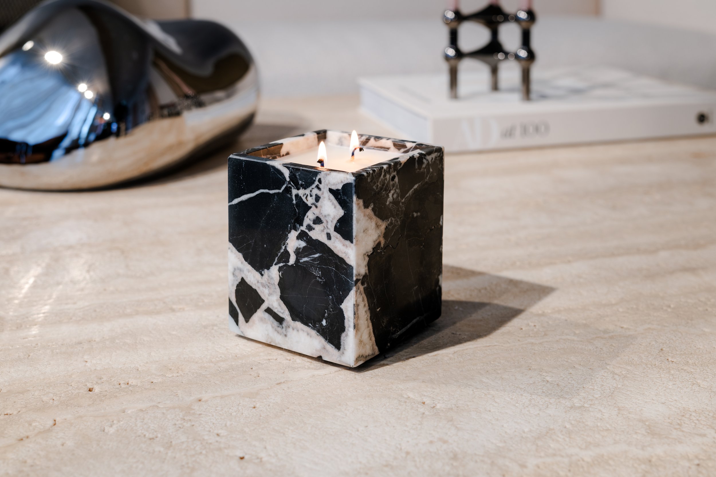 A lit black and white marble candle on a light-colored wooden surface, with a metallic object and a white book in the background.
