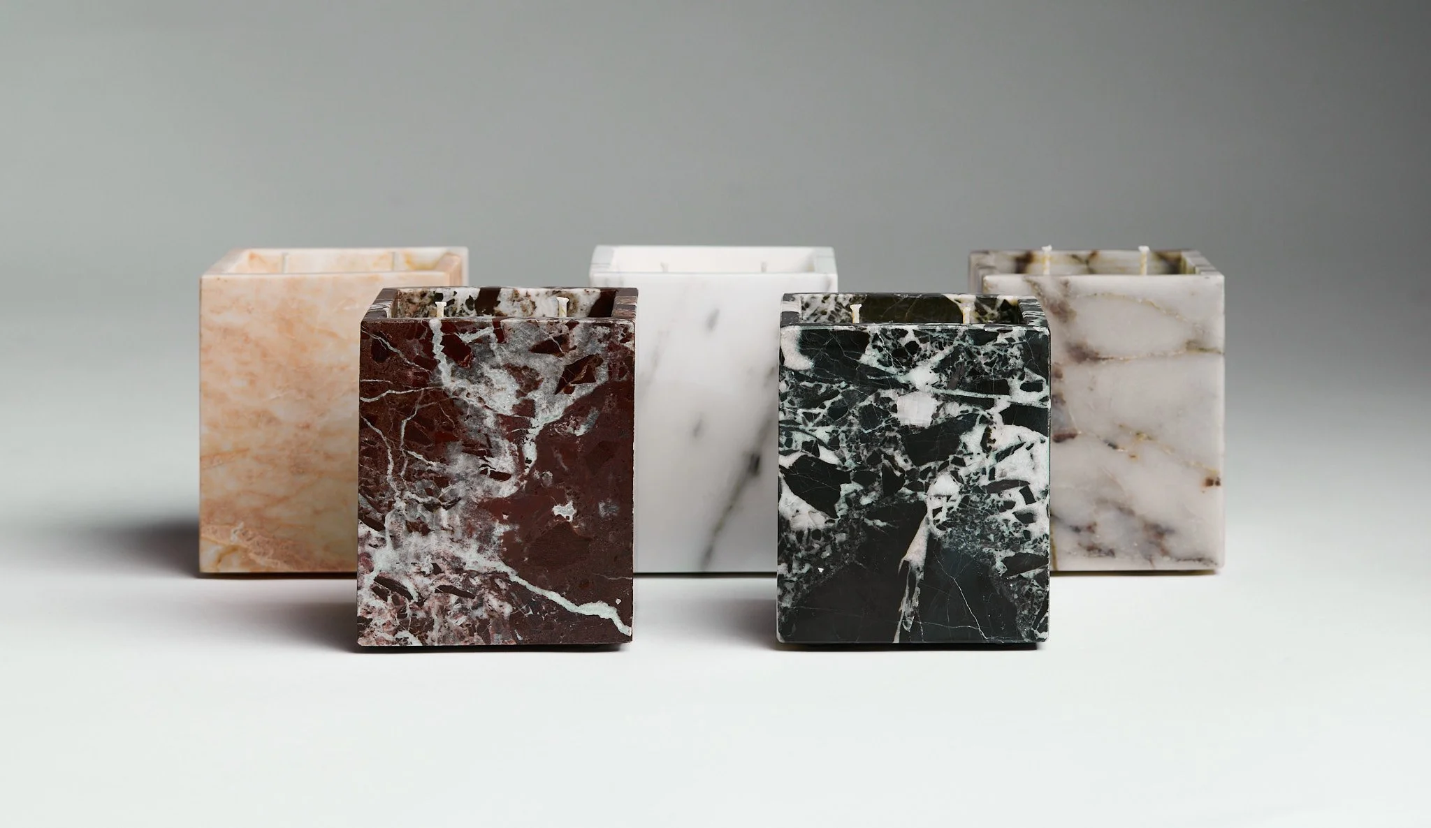 Five marble planters with different colors and patterns on a plain, light gray background.