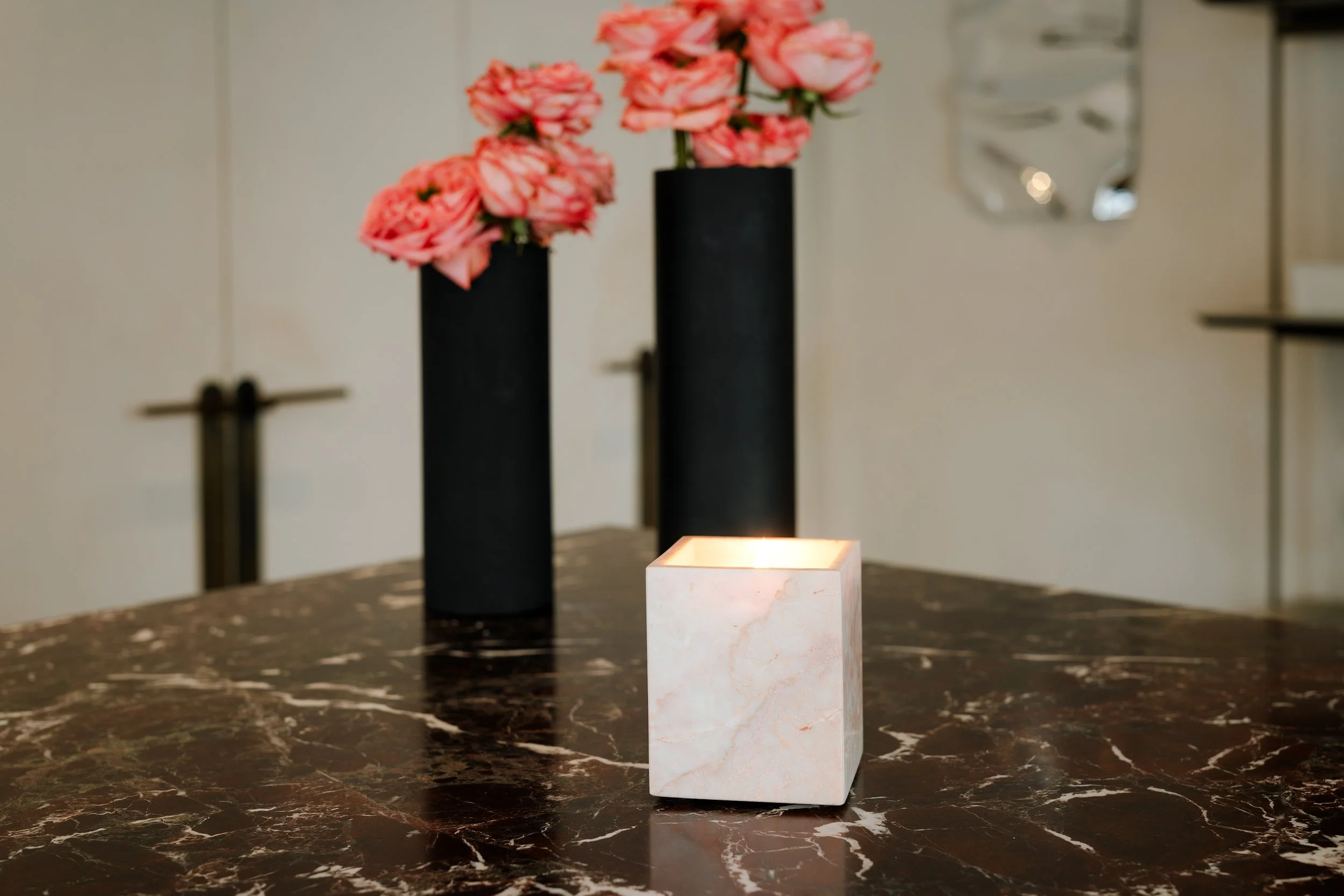 Close-up of a black marble table with a white marble cube and two black vases with pink and white flowers in the background.