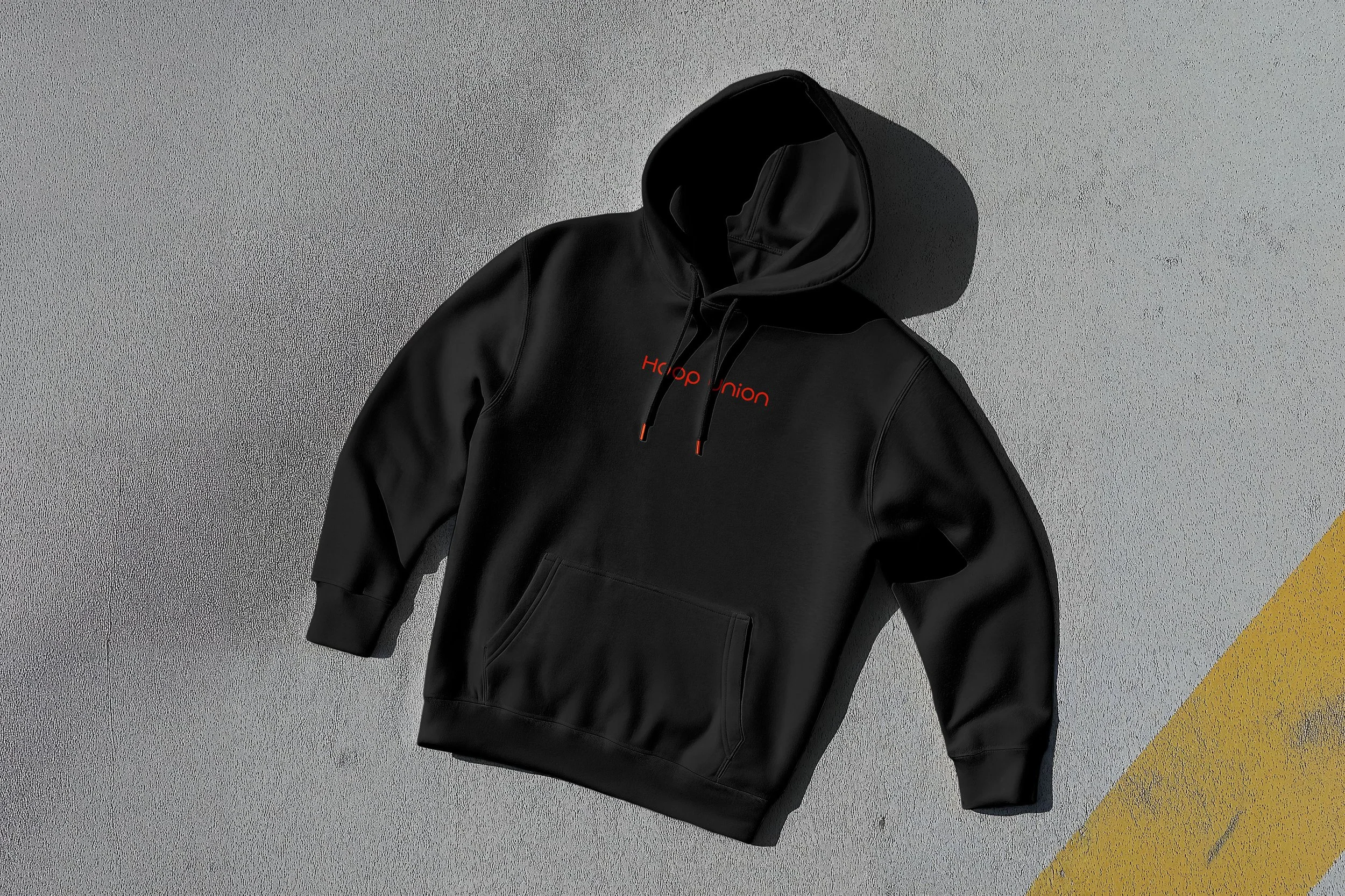 A black hoodie with red text says 'Hood Union' and is laid flat on a textured surface with a yellow line in the corner.