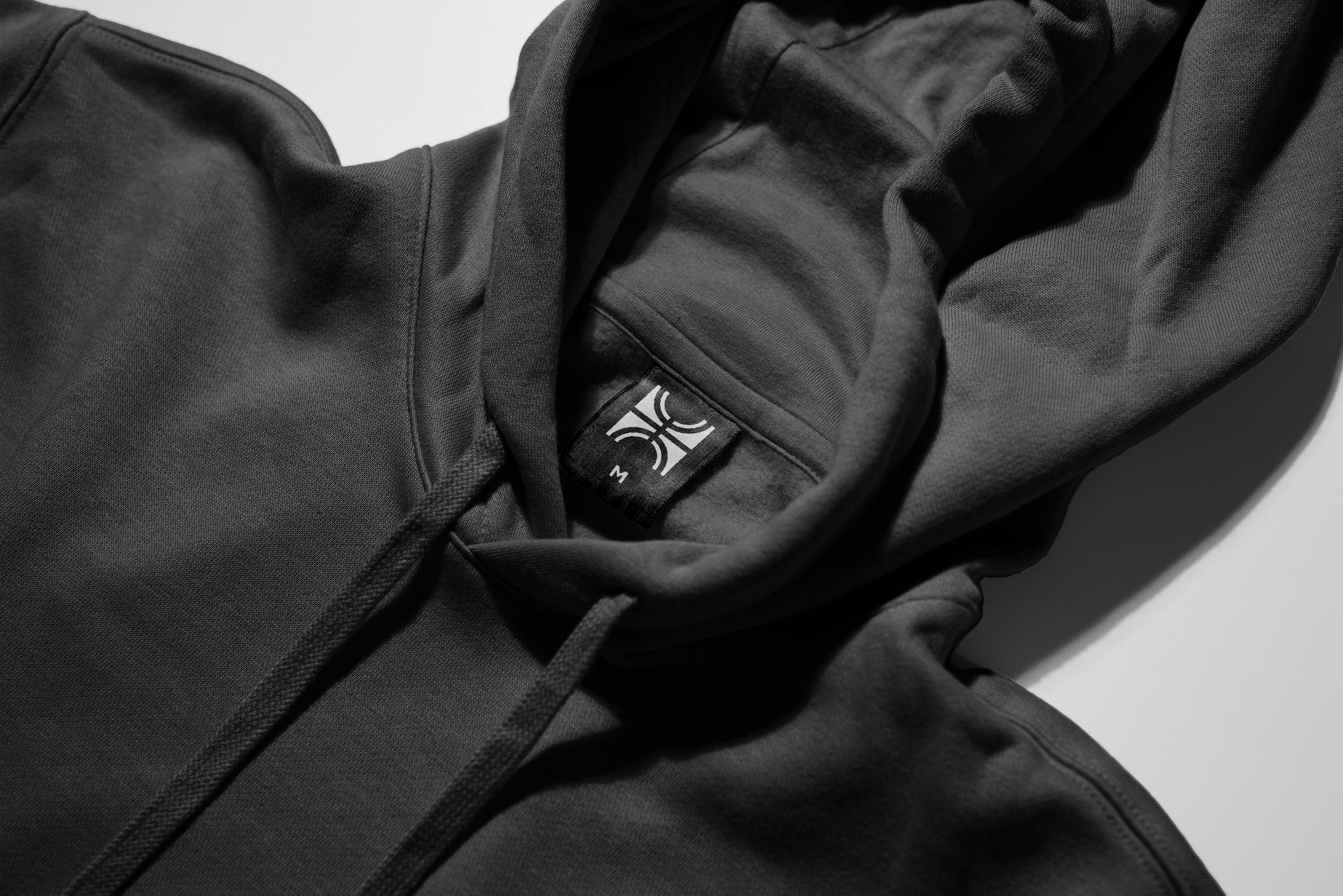 Close-up of a black hoodie with a tag showing a logo and the letter M.