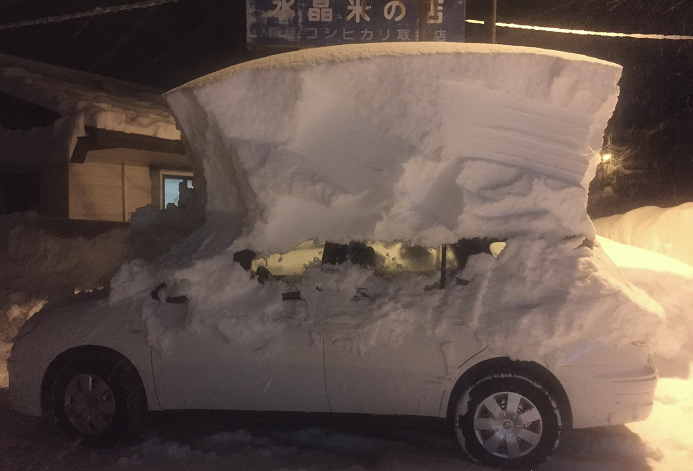 Car covered in a large snow shelter that extends above the vehicle, with snow piled on top and around the sides.