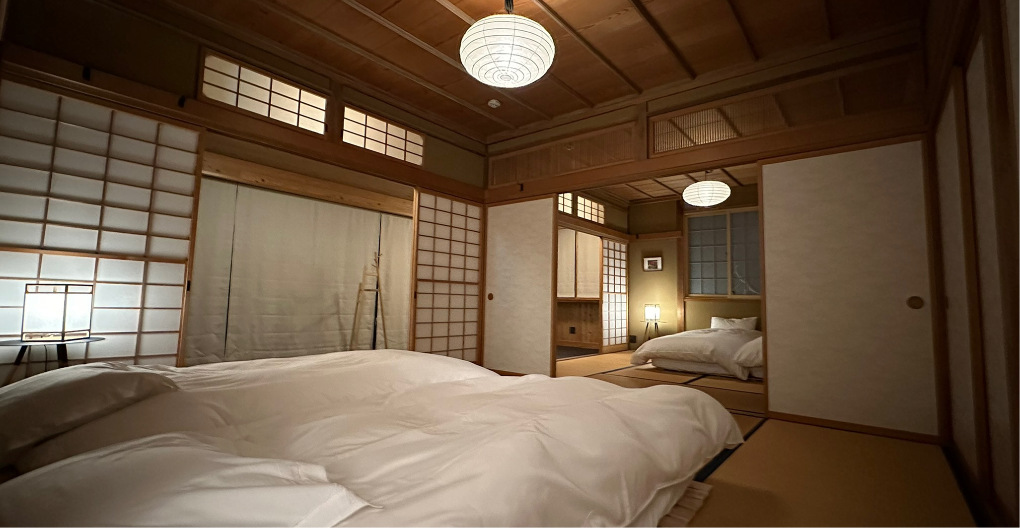 A traditional Japanese-style bedroom with tatami mats, sliding shoji screens, low beds, and paper lantern lighting.