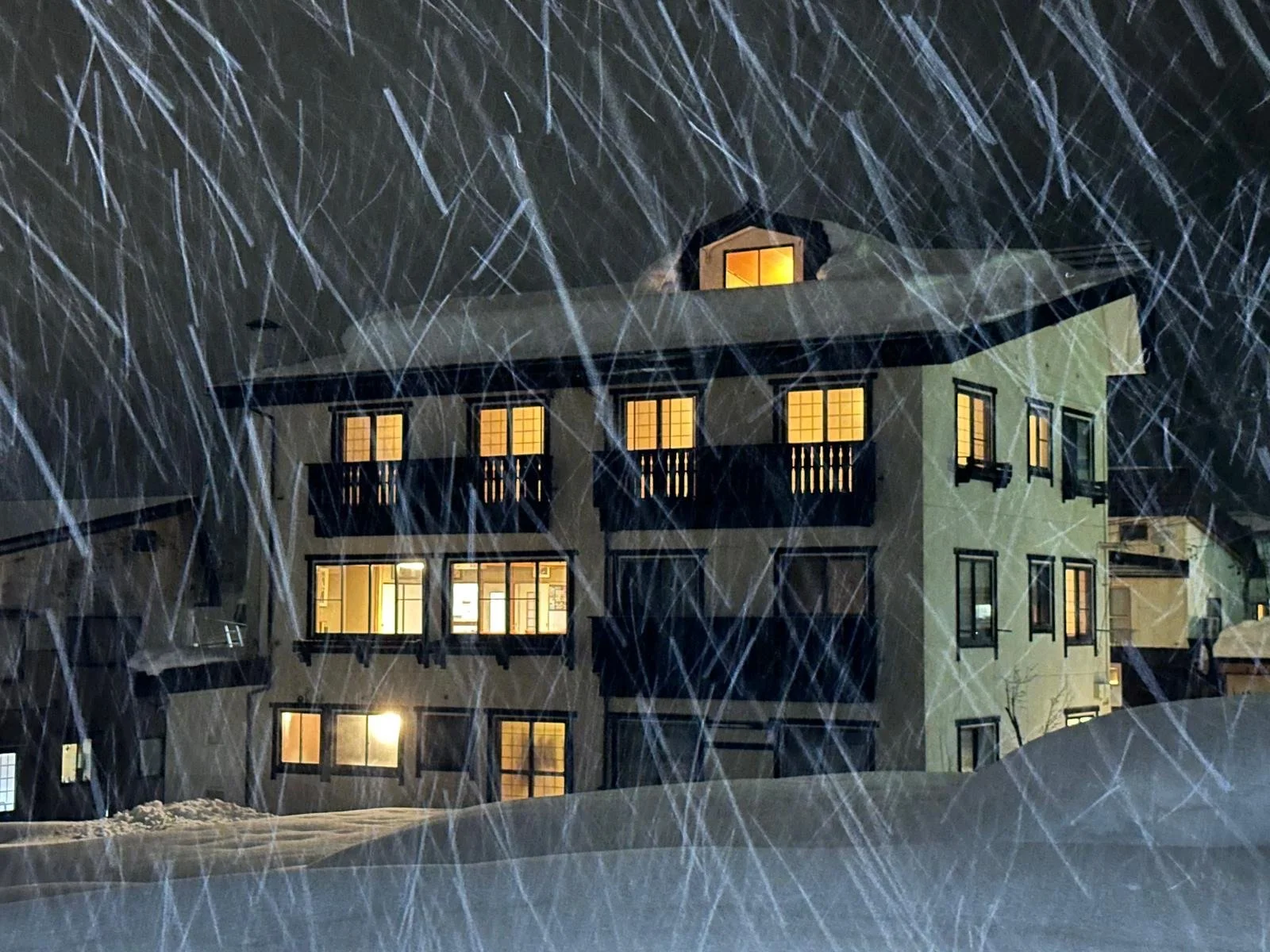 A multi-story house with lit windows during a heavy snowstorm at night.