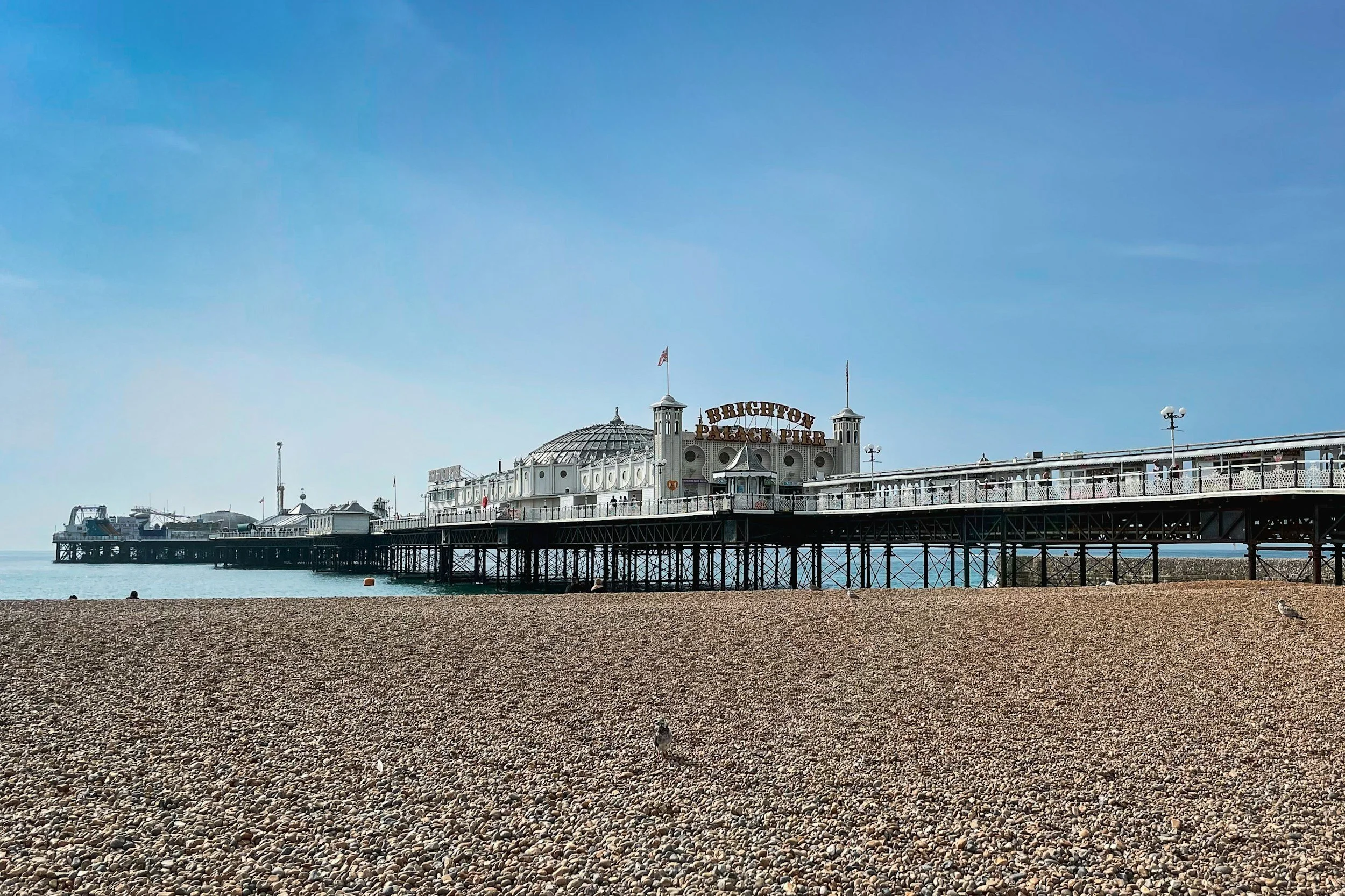 Brighton Palace Pier with a clear blue sky, situated above a pebbled beach.