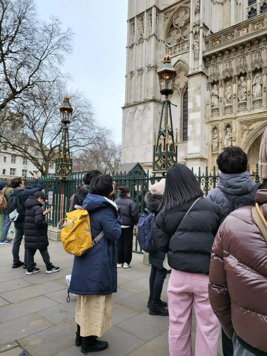 Tourists and visitors standing outside a historic cathedral with intricate stone carvings, likely Westminster Abbey, in London, UK.