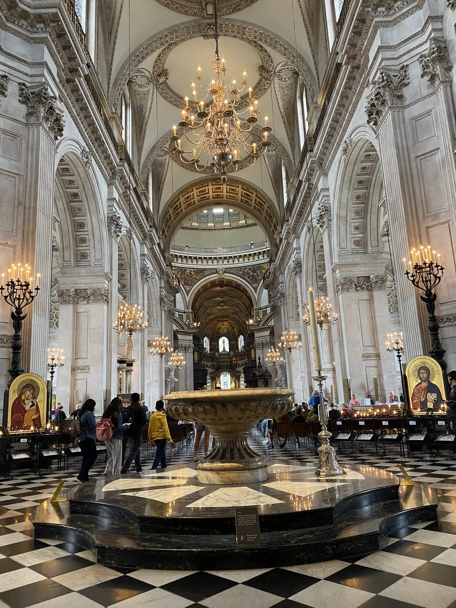 Inside a grand, ornate church with high vaulted ceilings, large chandeliers, marble accents, and religious icons, with visitors walking around.