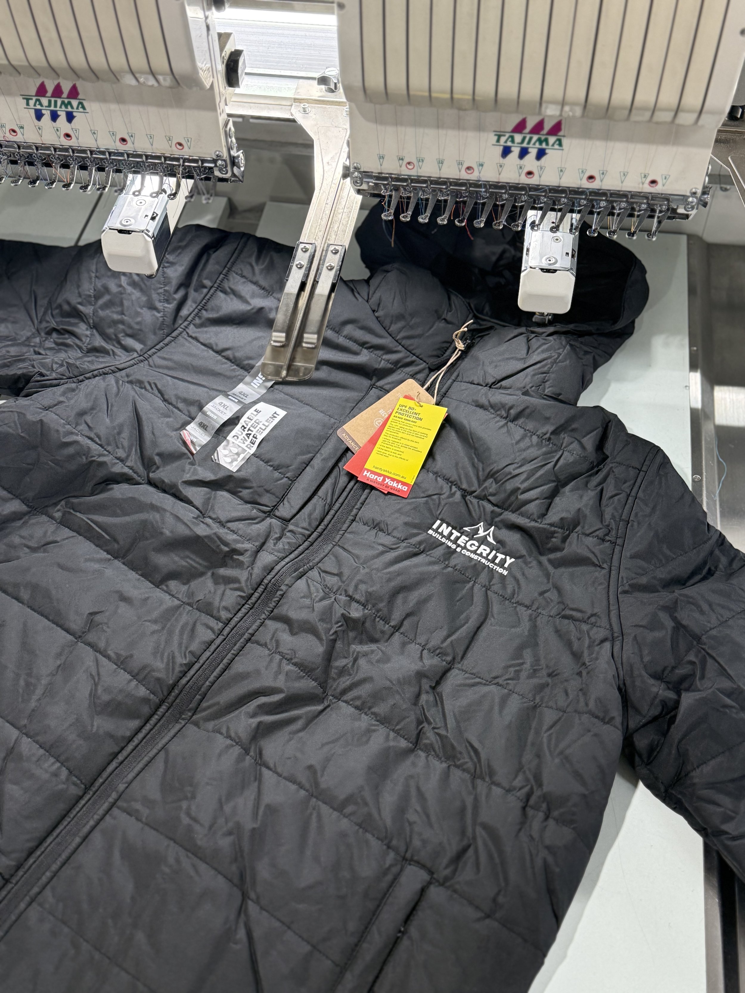 Black quilted insulated jacket with tags, lying on a conveyor belt in a manufacturing or inspection process.