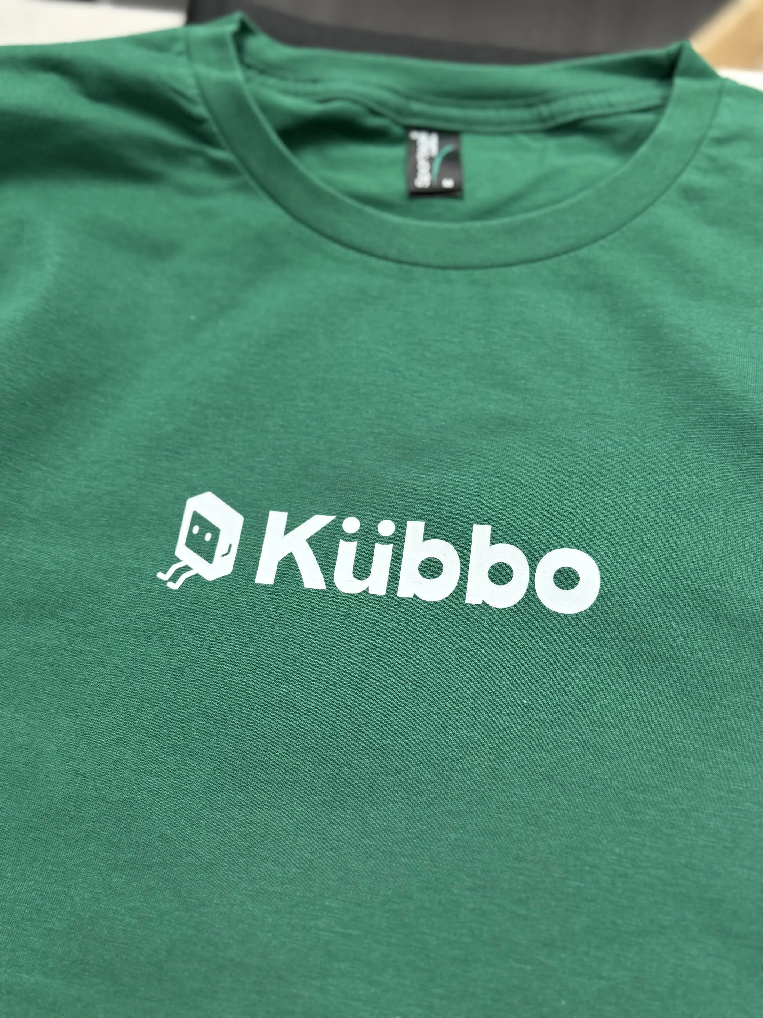 Green T-shirt with a white logo and text 'Kübbо' on it.