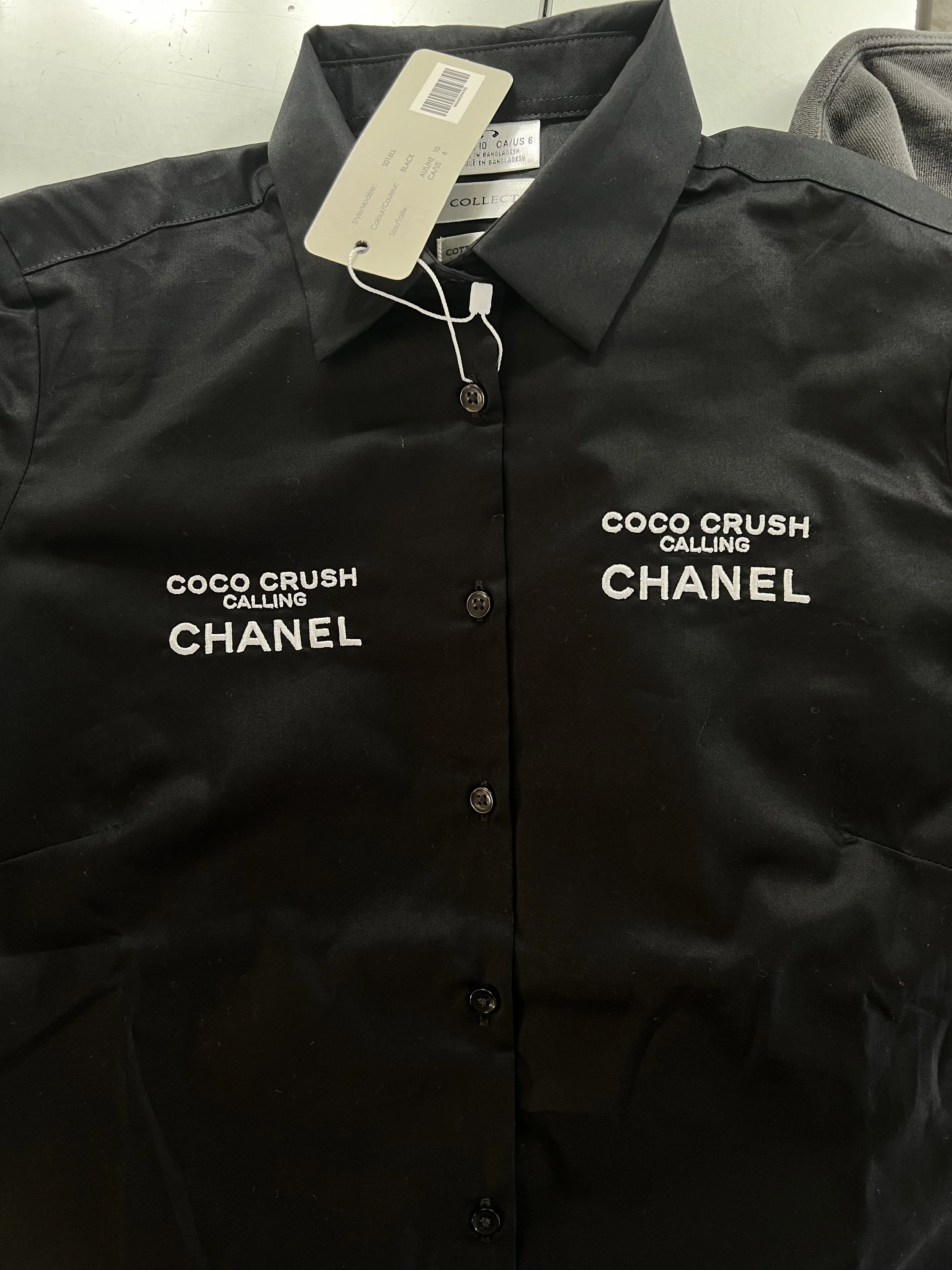 Black button-up shirt with white embroidered text reading 'COCO CRUSH CALLING CHANEL' on the left and right chest.
