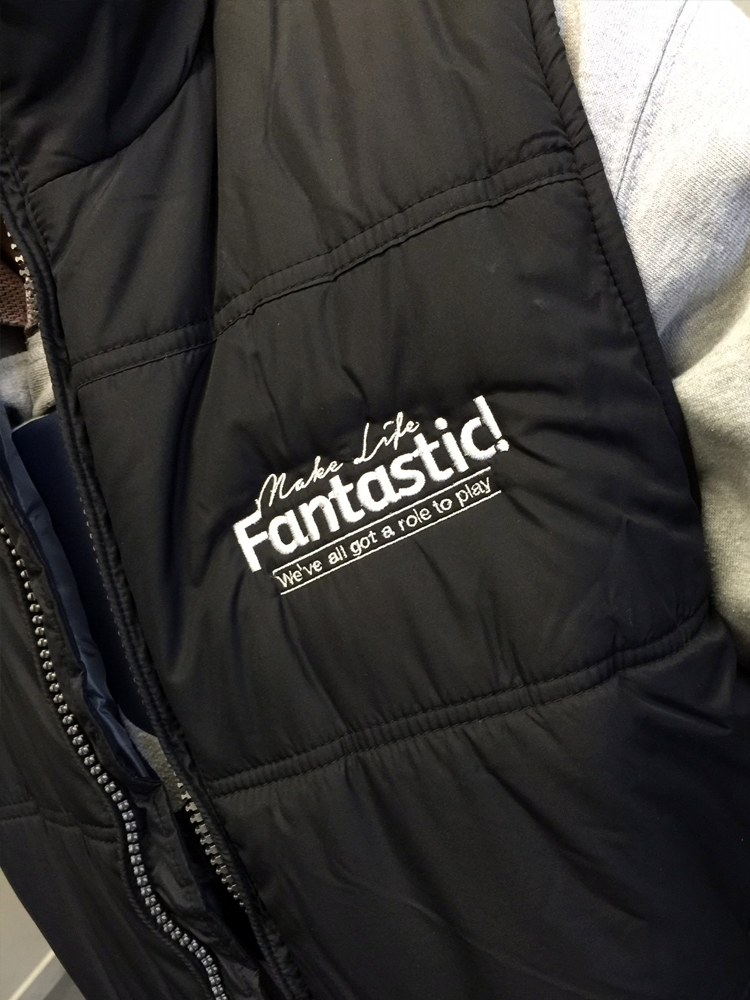 Close-up of a black jacket with white embroidered text that reads "Make Life Fantastic! We've all got a role to play."