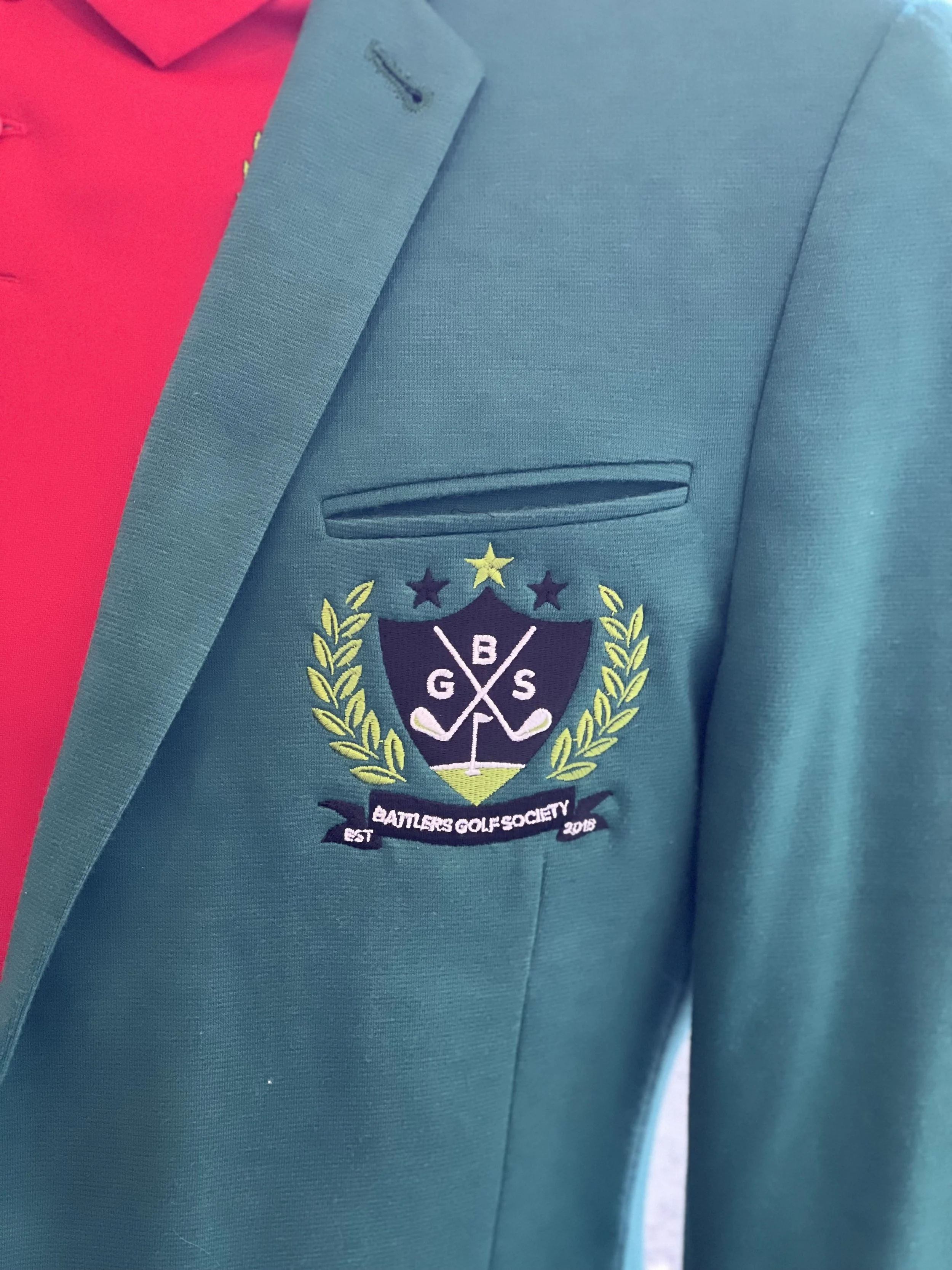 Close-up of a formal green blazer with an embroidered golf crest reading "Battleers Golf Society" on the chest pocket.