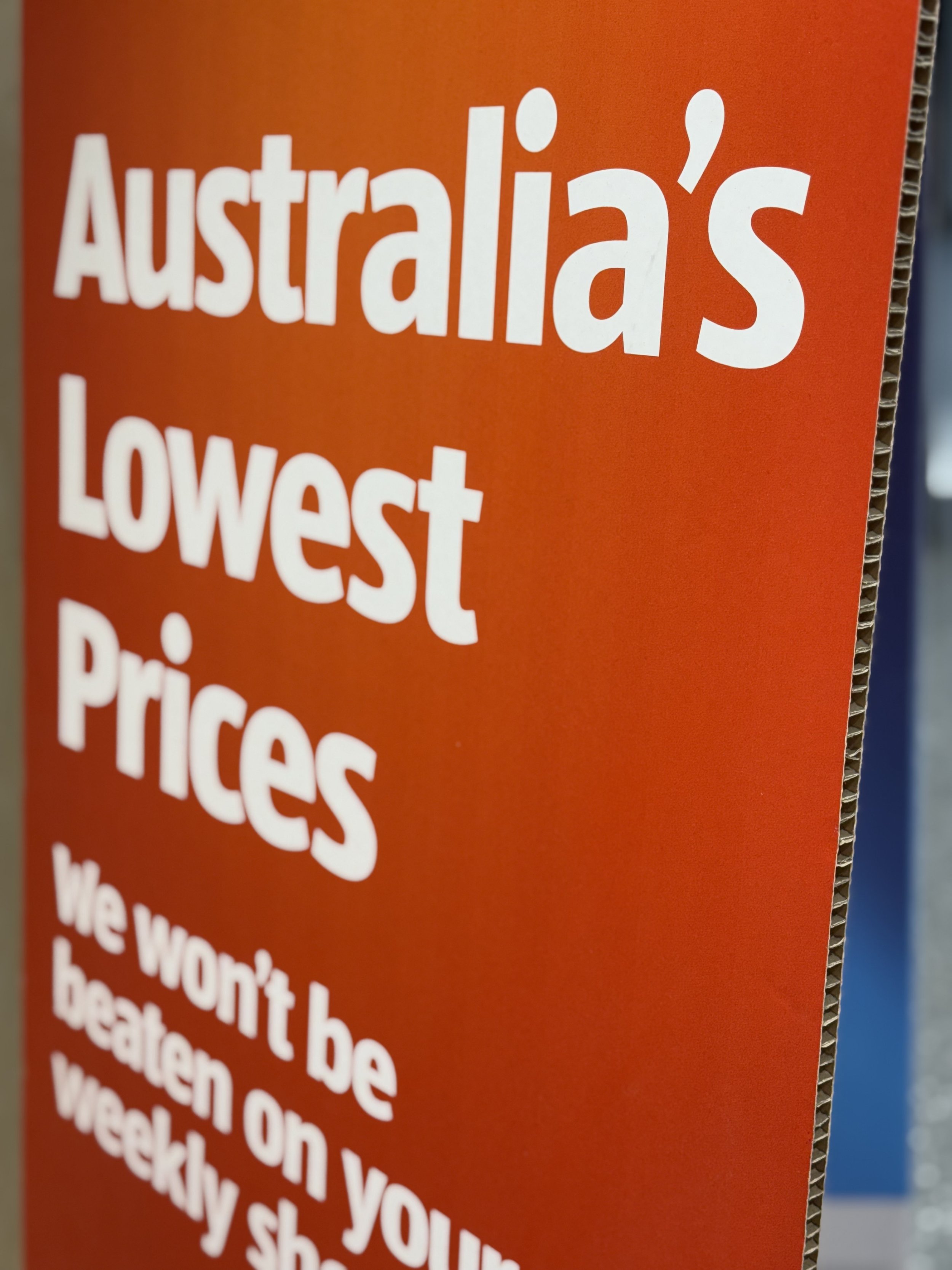 Close-up of a red sign with white text that reads "Australia's Lowest Prices" and additional smaller text below.
