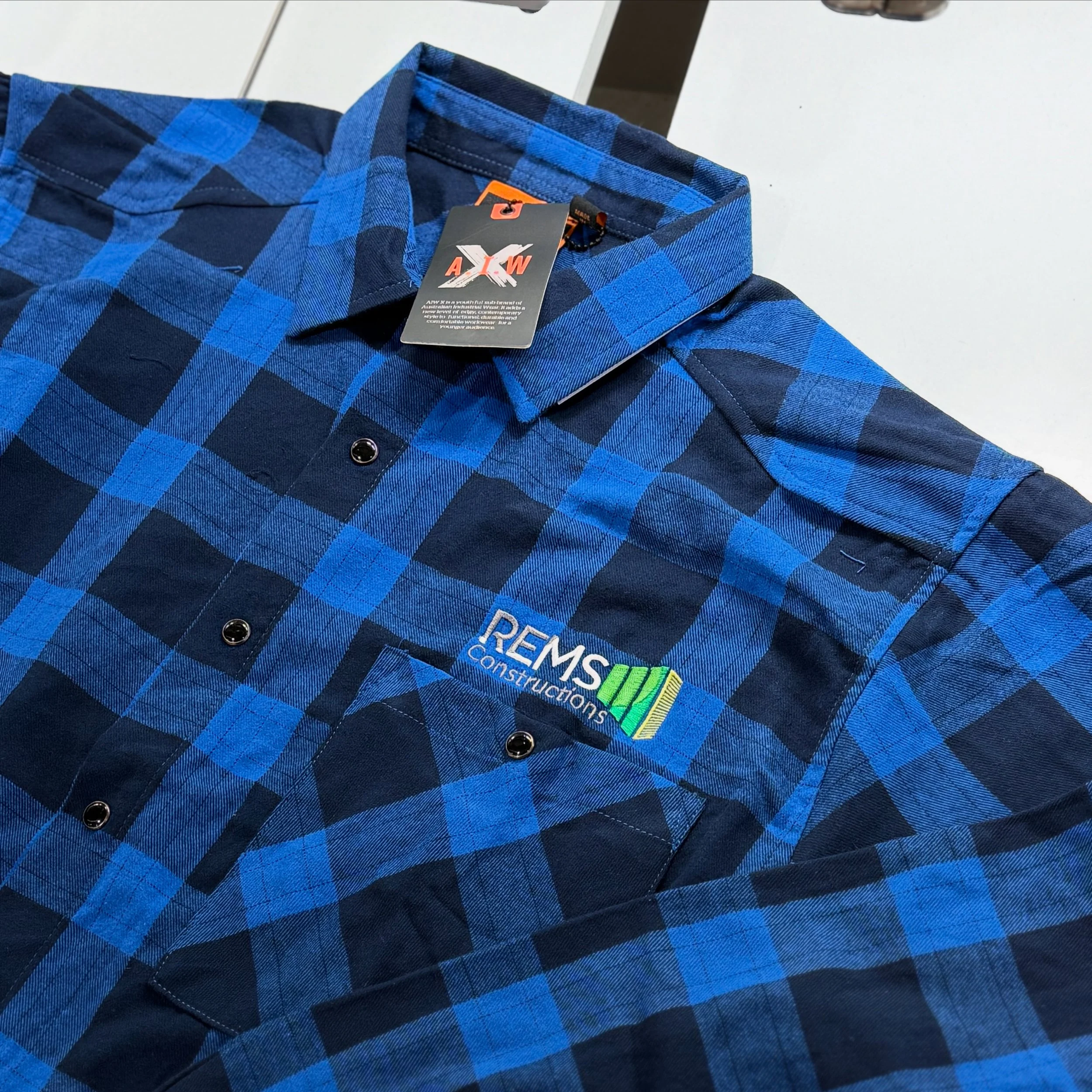 Blue and black plaid button-up shirt with 'REMSCONSTRUCTIONS' logo embroidered on the chest.