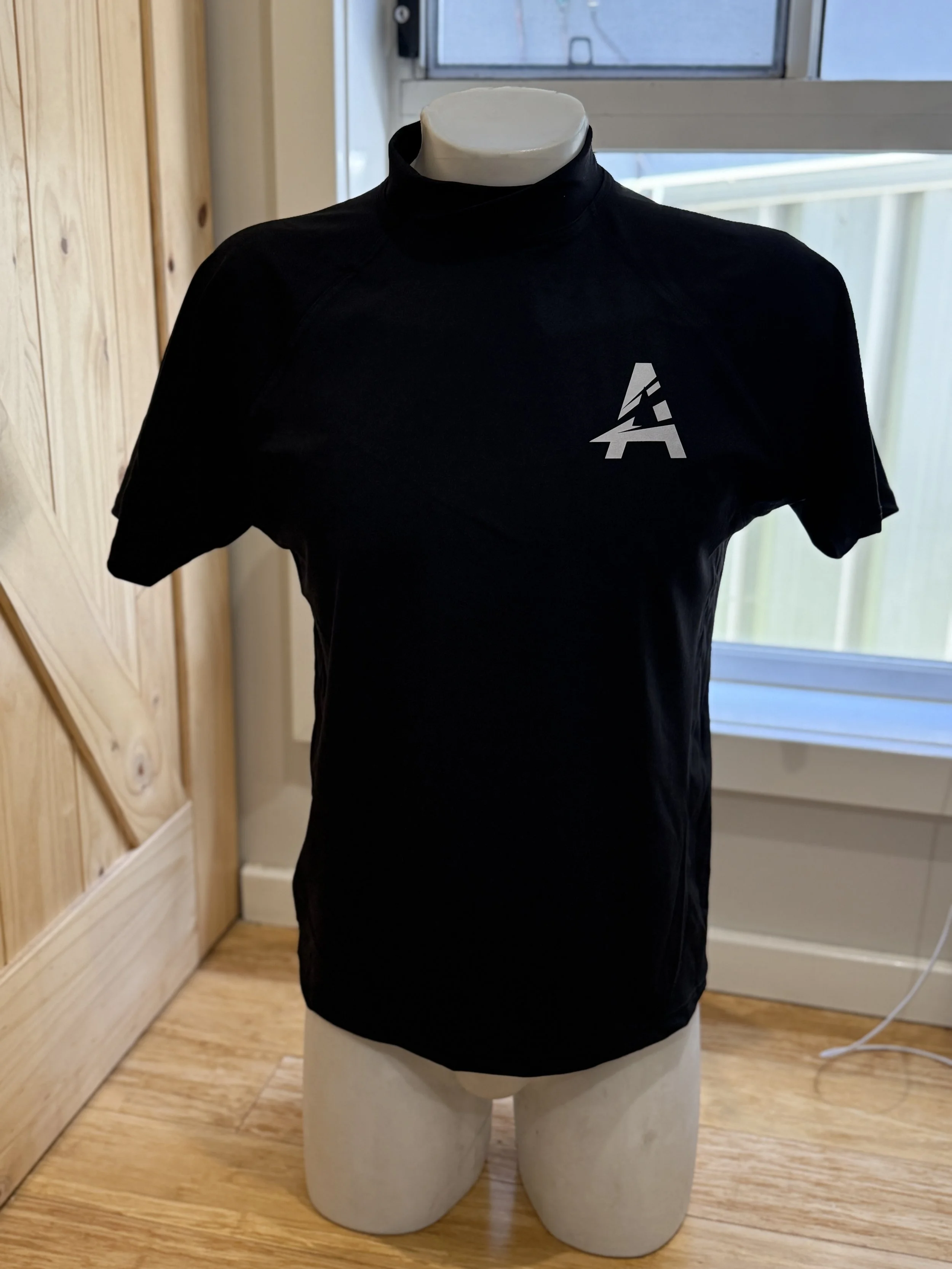 Black athletic shirt with a white logo on the left chest displayed on a mannequin torso.