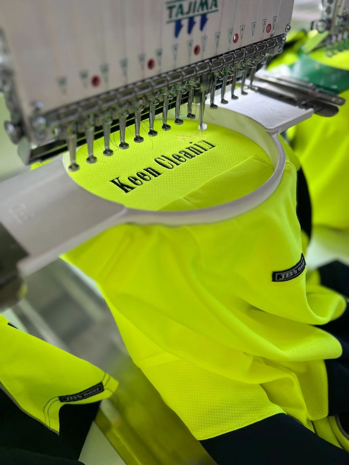 High-visibility yellow work gloves being embroidered with black text using a commercial embroidery machine.