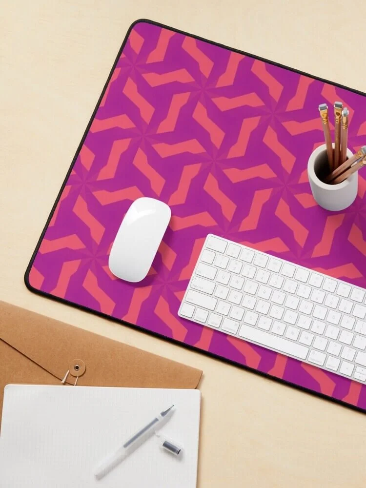 Desk with a colorful geometric patterned mouse pad, white wireless mouse, white keyboard, white cup holding pencils, envelope, notebook, and pen.