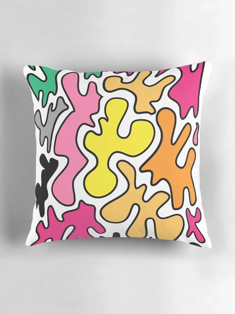 Colorful abstract patterned pillow with irregular shapes in pink, yellow, orange, green, black, and white on a gray background.