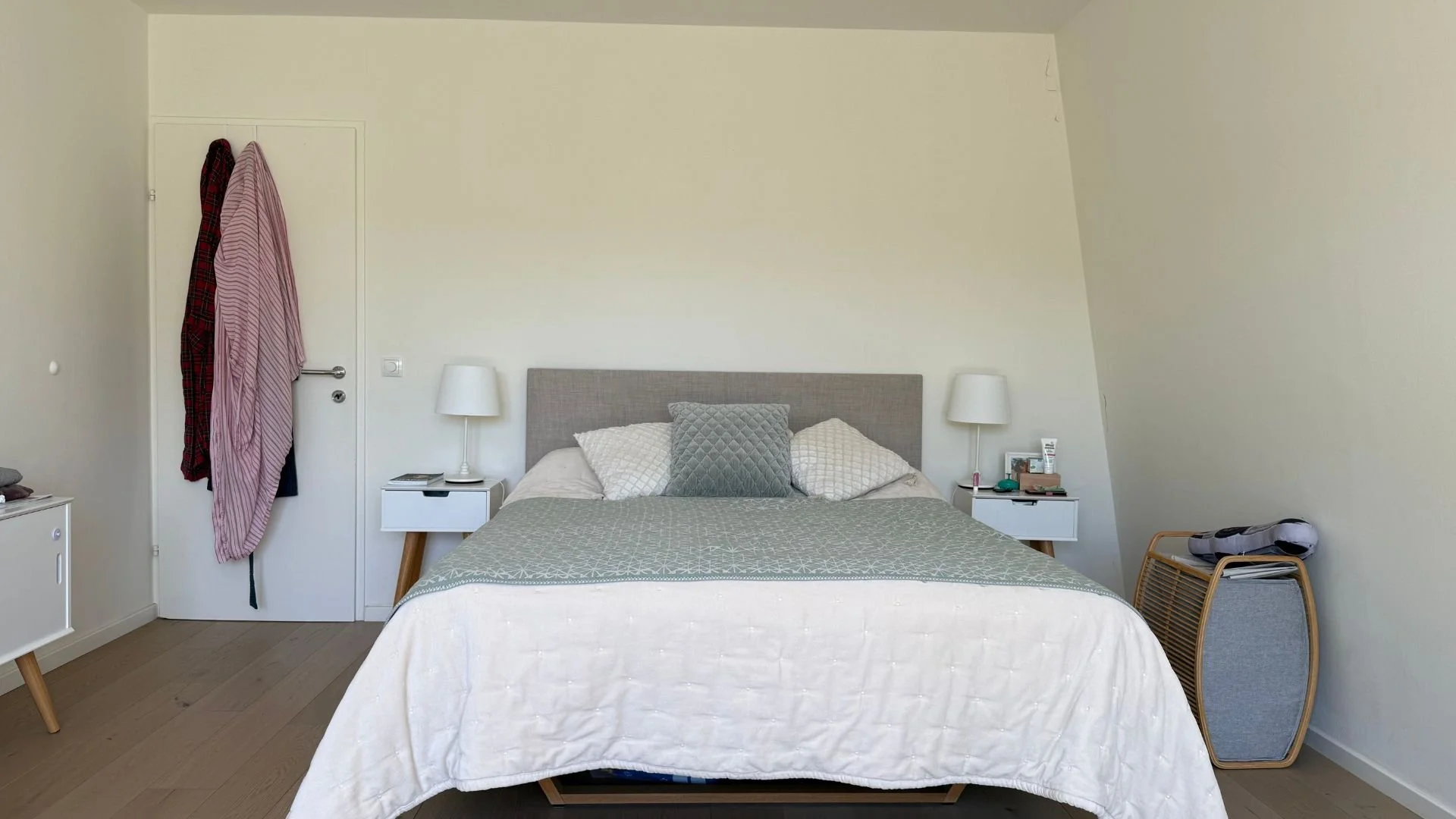 Schlafzimmer vor der Neugestaltung mit Polsterbett, weißen Nachtkästchen und kahler Wand unter der Dachschräge.