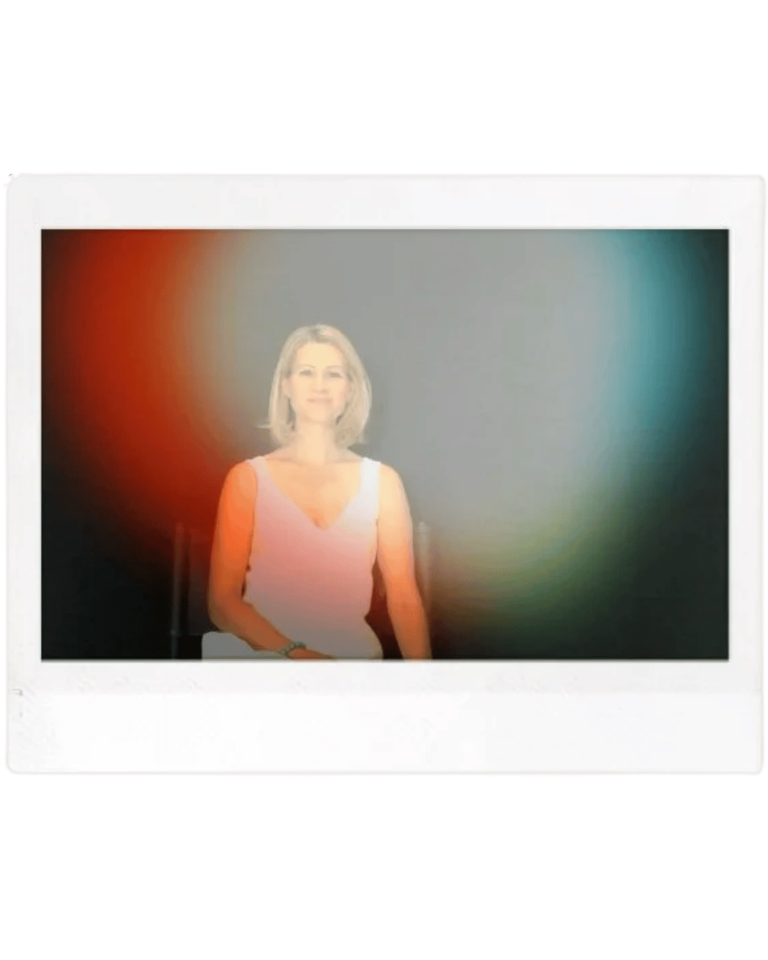 A woman with blonde hair sitting on a chair in front of a dark background with red, yellow, and teal light flares.