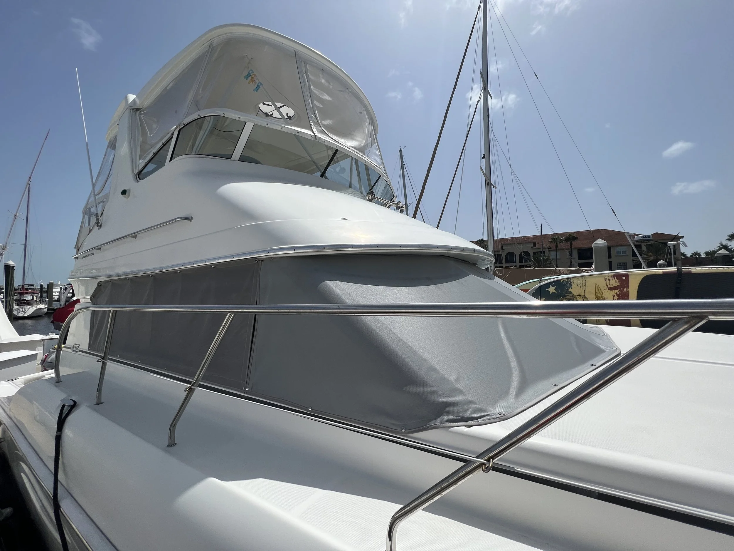 White yacht docked at marina with sailboats and blue sky in background.