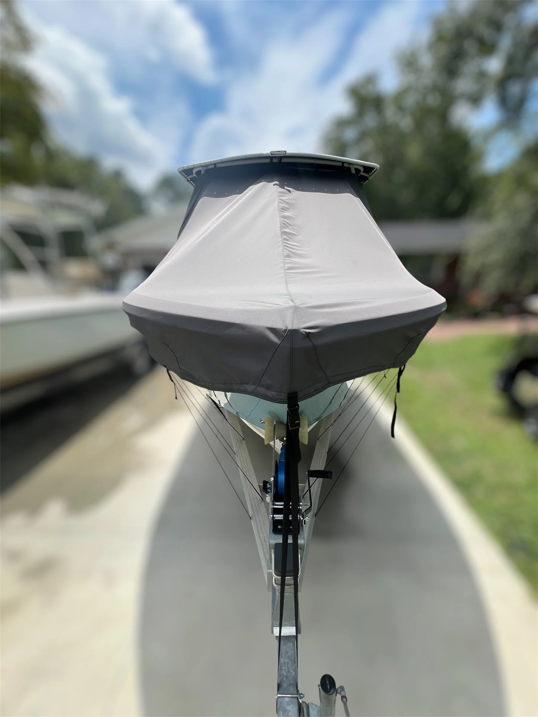 Front view of a boat with a covered bow, on a trailer, parked on a concrete driveway.
