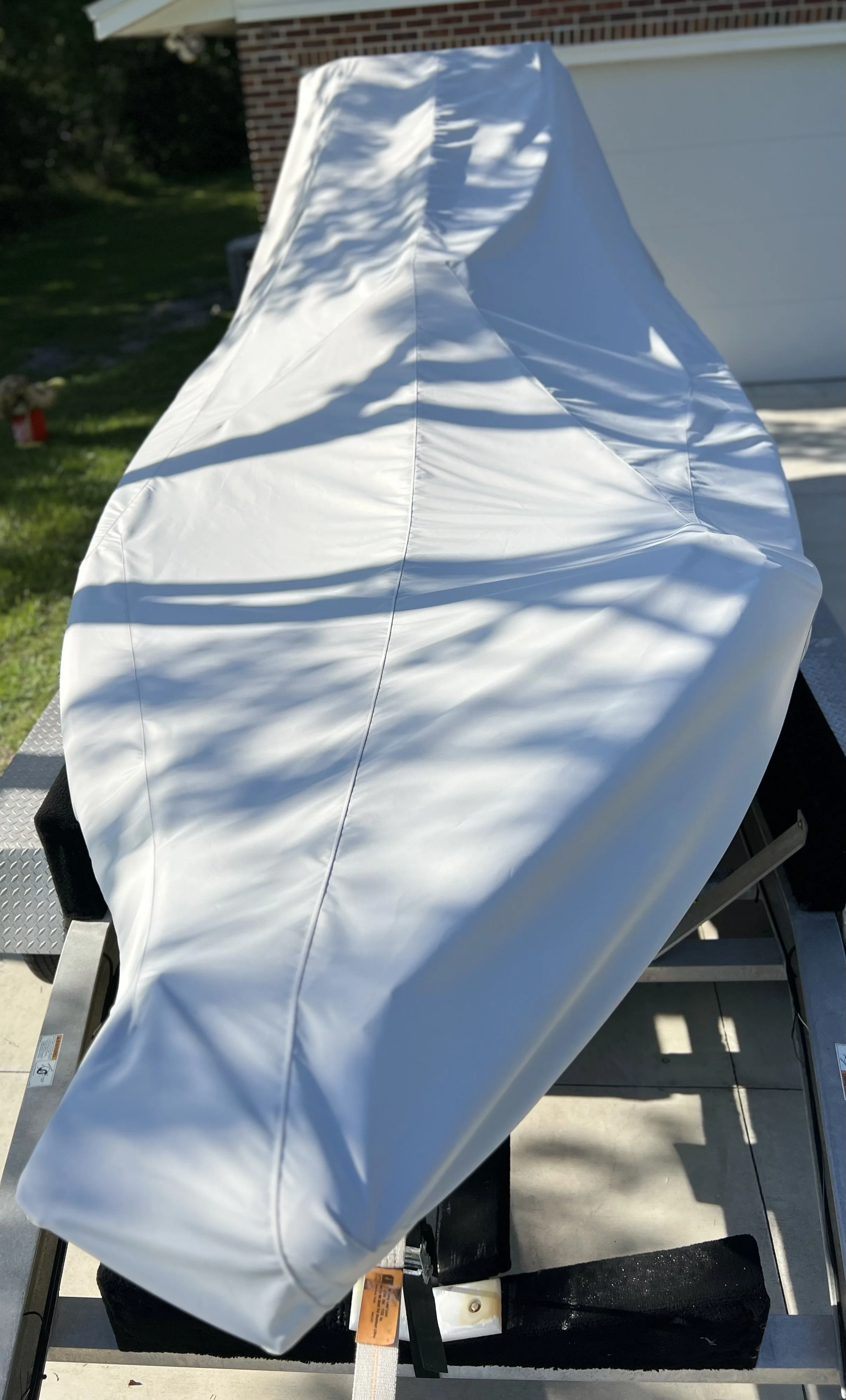 A boat covered with a white protective cover, placed on a trailer in a driveway.