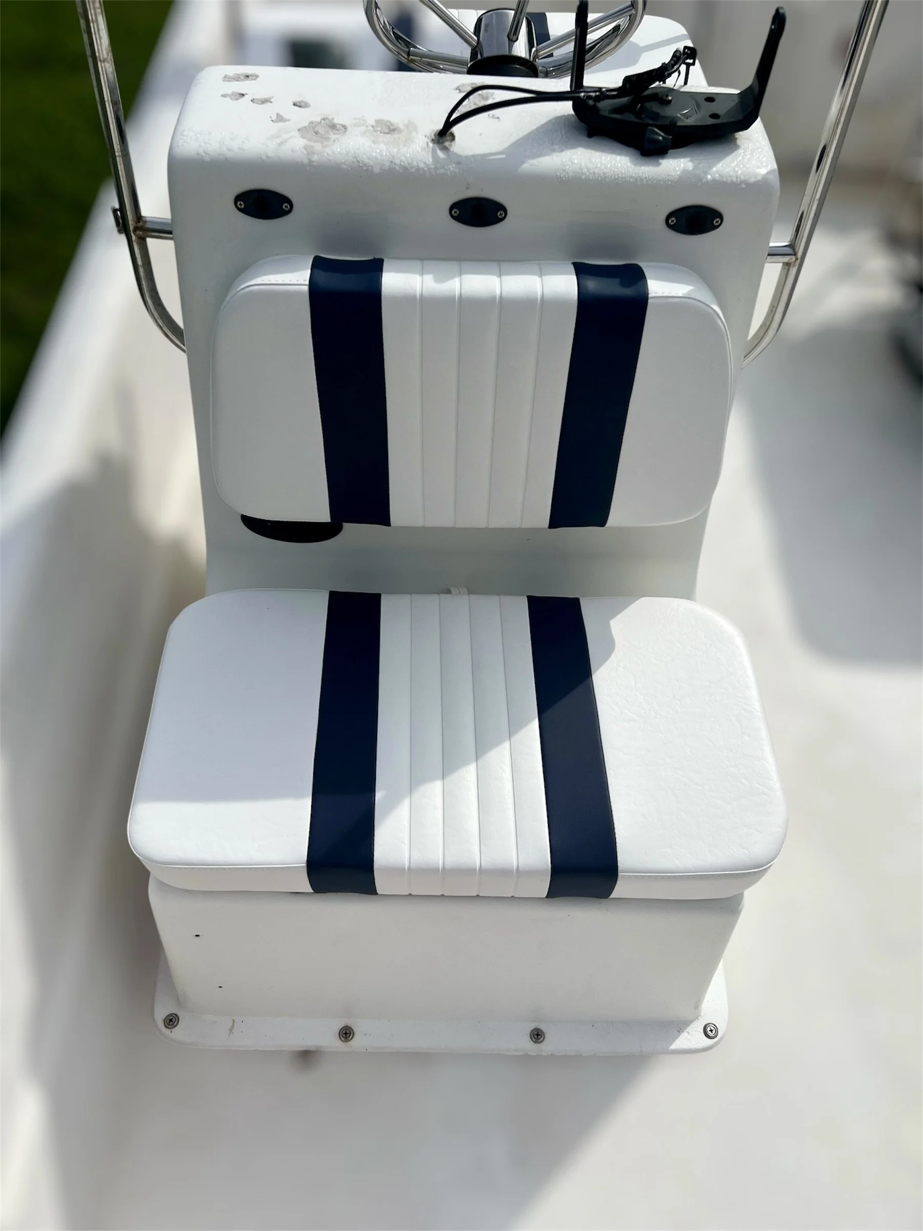Close-up of a white boat seat with navy blue stripes, attached to a white boat interior. The background shows some greenery.