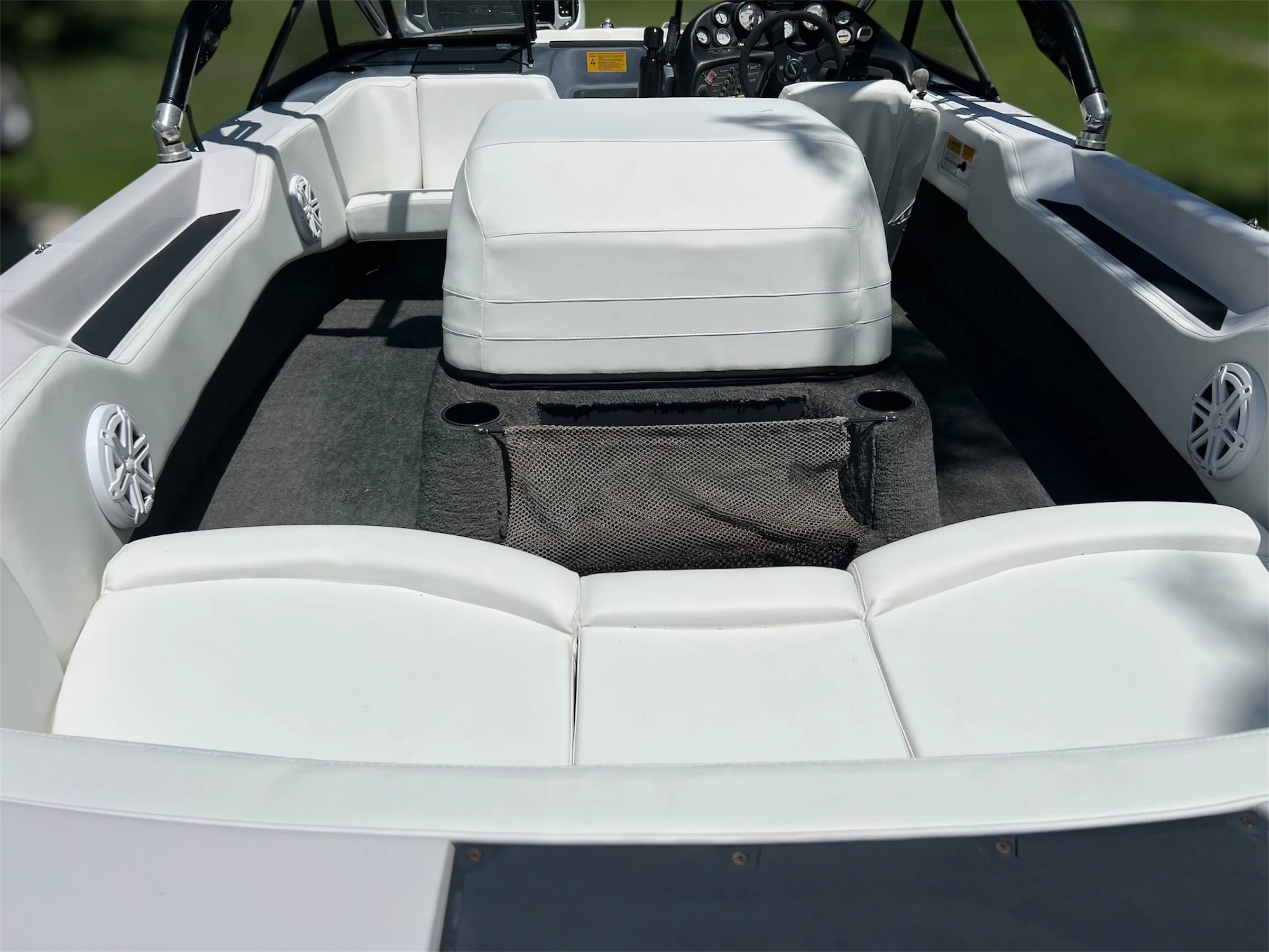 The interior of a white motorboat with white cushioned seating, a dashboard with gauges, and built-in speakers.