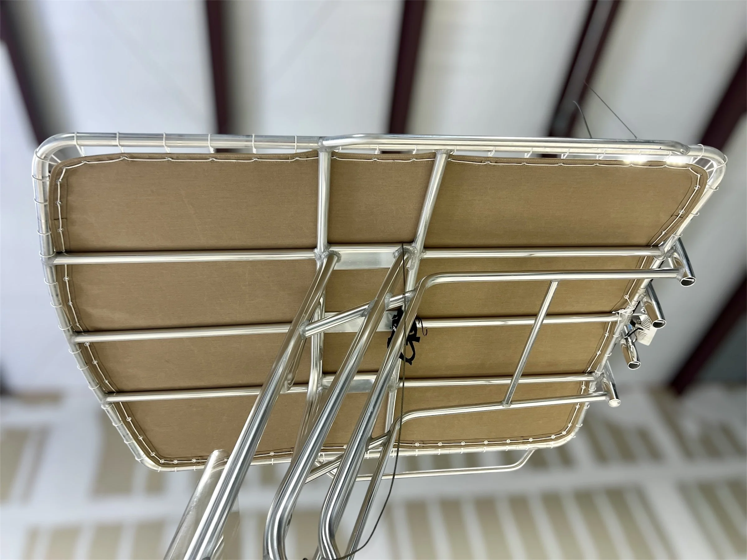 A close-up of a shopping cart with a brown cardboard bottom shelf, taken from below, showing the metal frame and wheels inside a store.