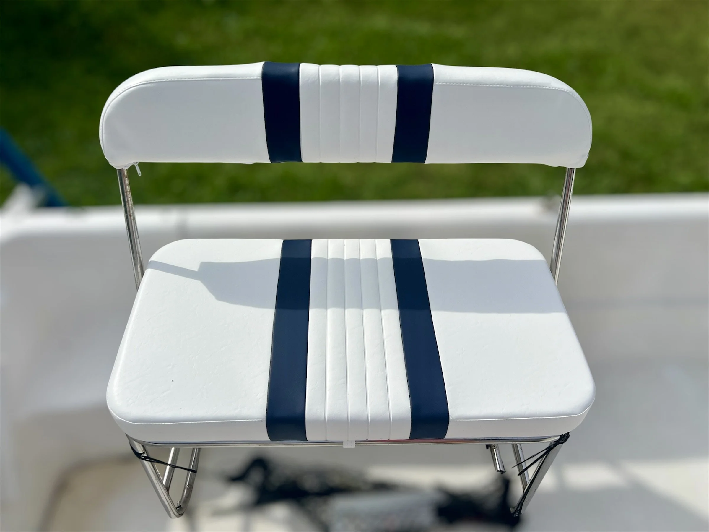 Close-up of a white stadium or boat chair with blue stripes, set against a background of green grass.