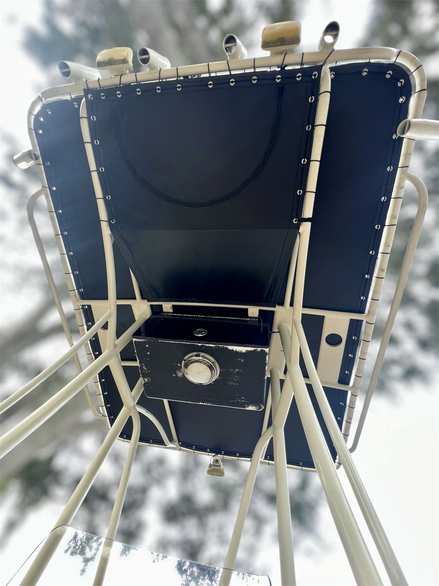 Looking up at a blue and white lifeguard tower from below, with a cloudy sky and trees in the background.
