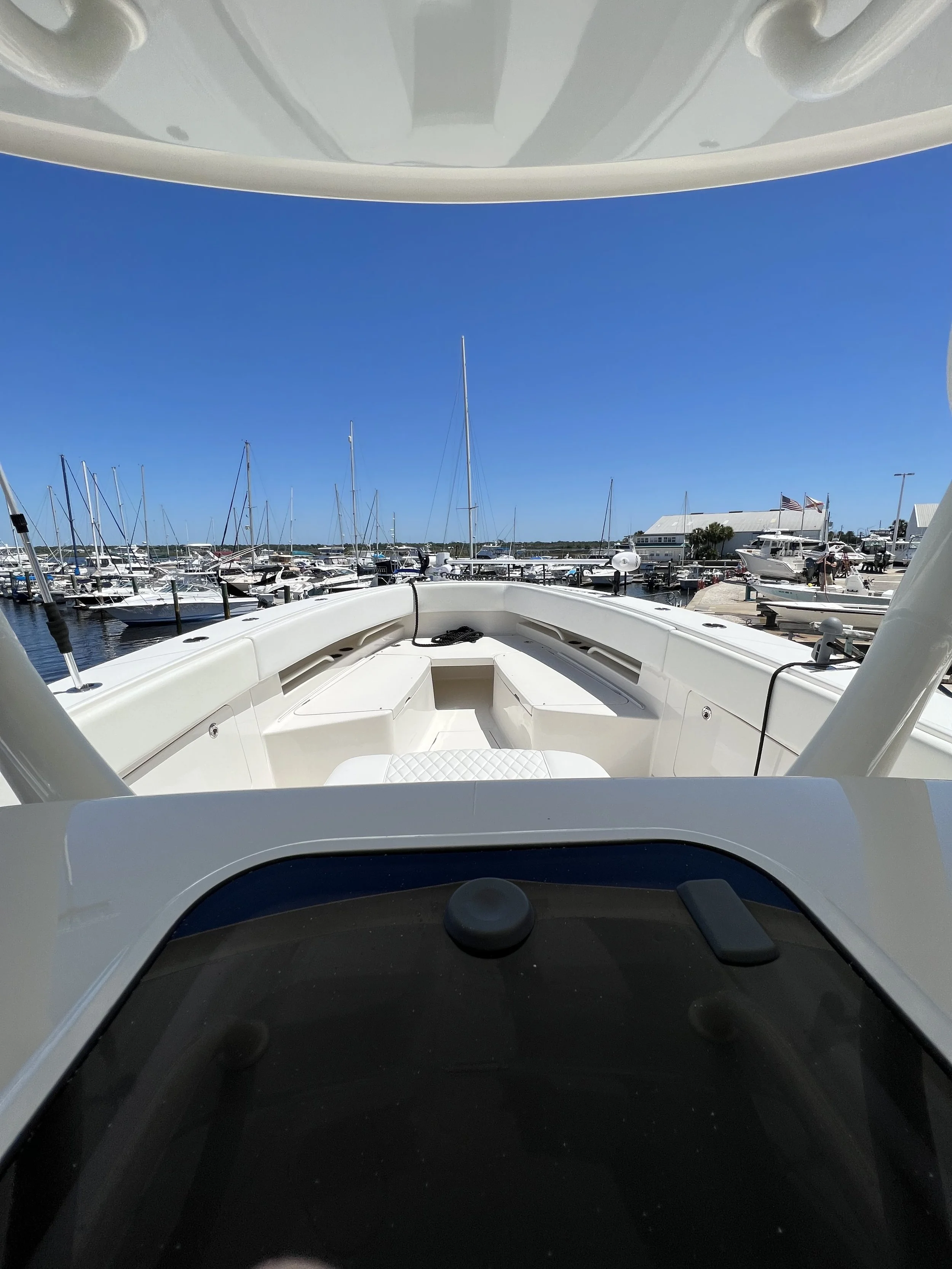 View from the cabin of a white yacht looking out towards a marina with several sailboats and motors boats docked, under a clear blue sky.