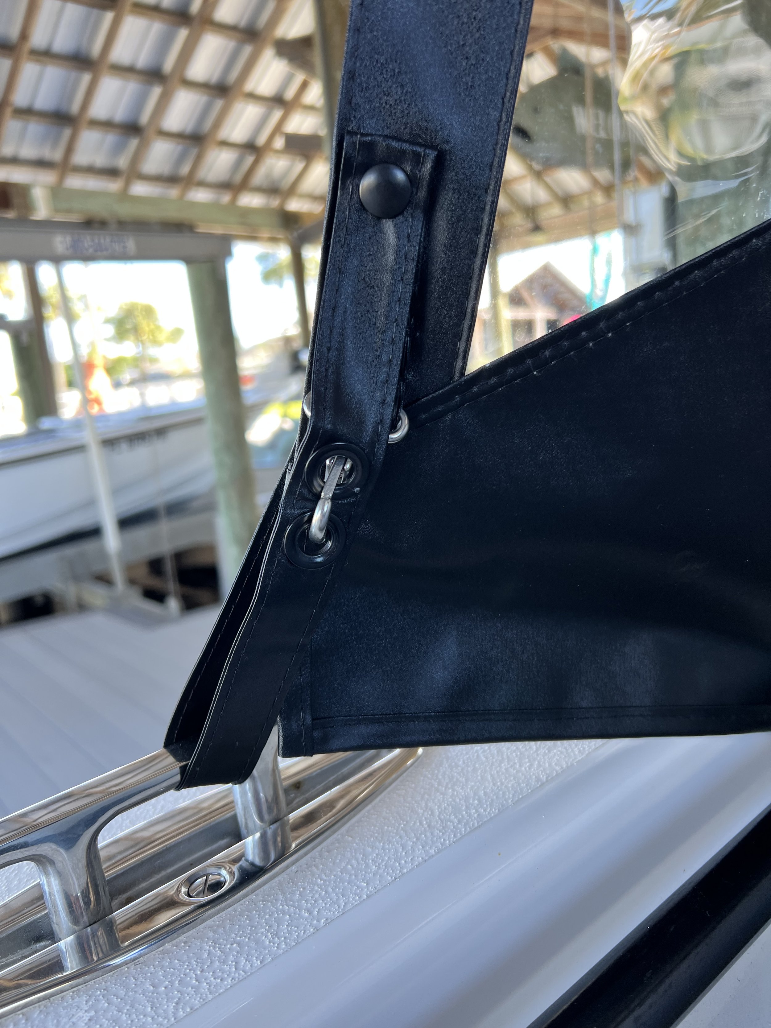 Close-up of a boat canopy frame with metal fasteners and glass windshield, showing a marina in the background.