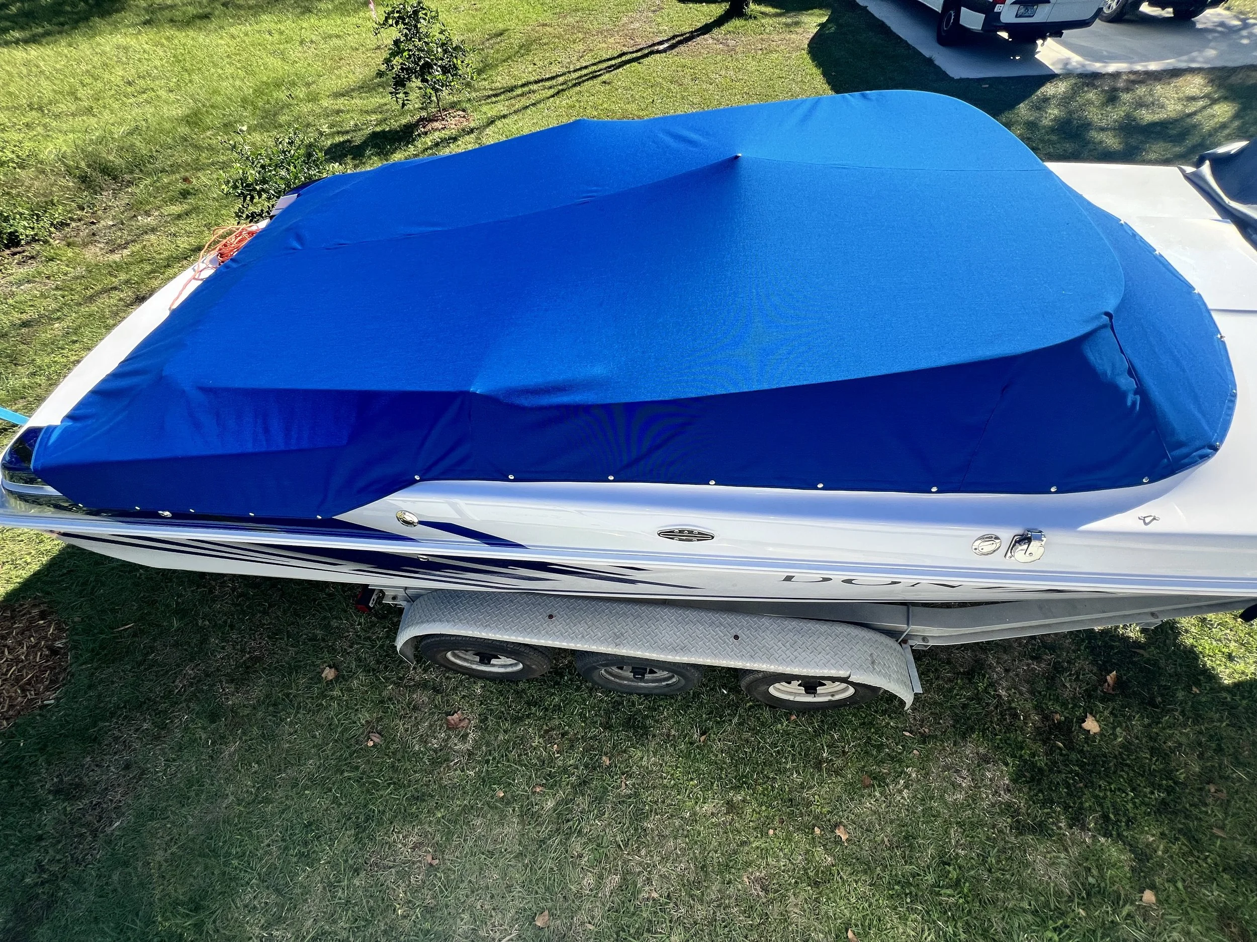 A white speedboat with a blue cover on top, parked on a trailer on a grassy area.
