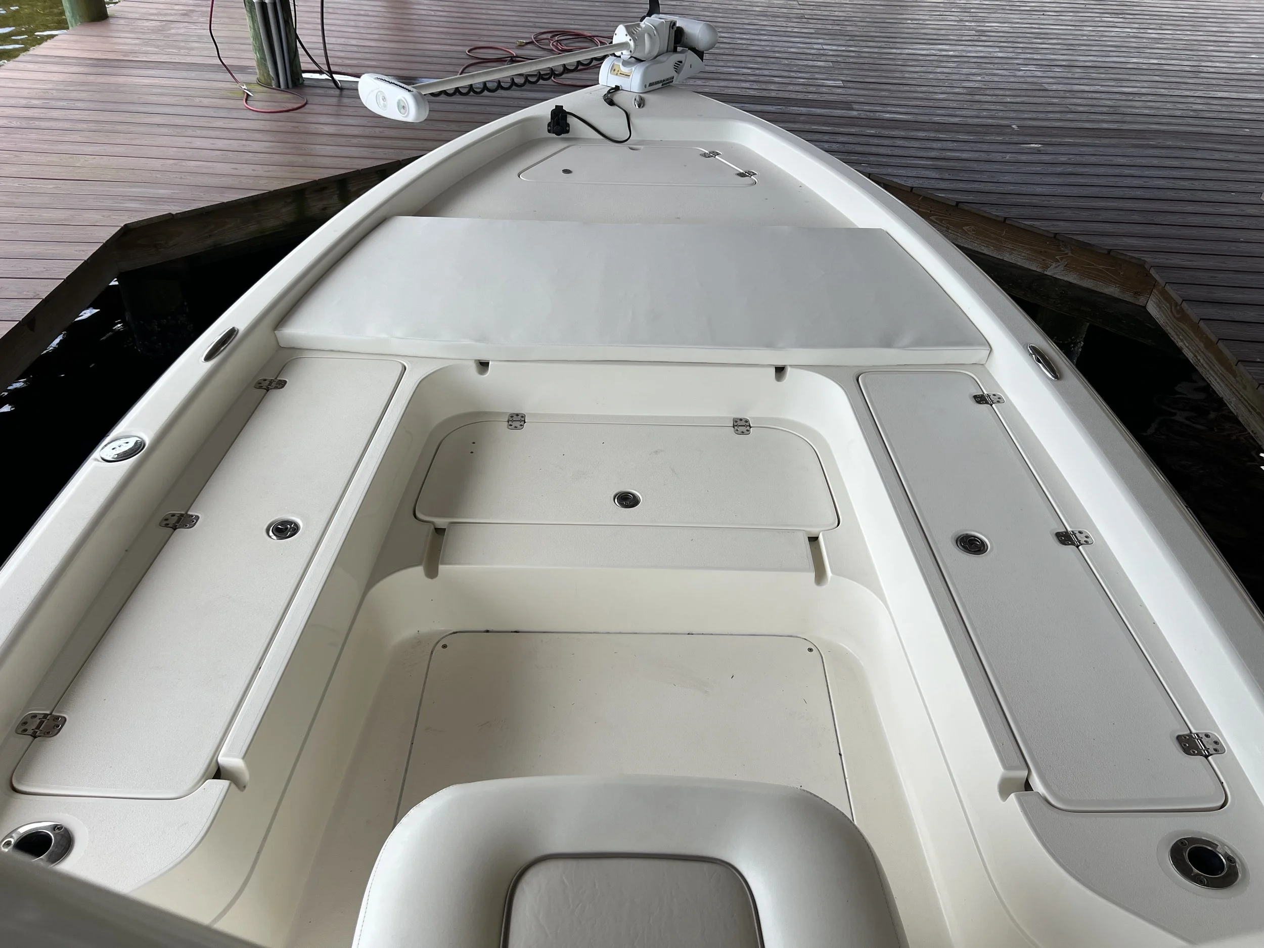 The interior of a white fishing boat with storage compartments, a seating area, and a steering mechanism visible, docked next to a wooden pier.