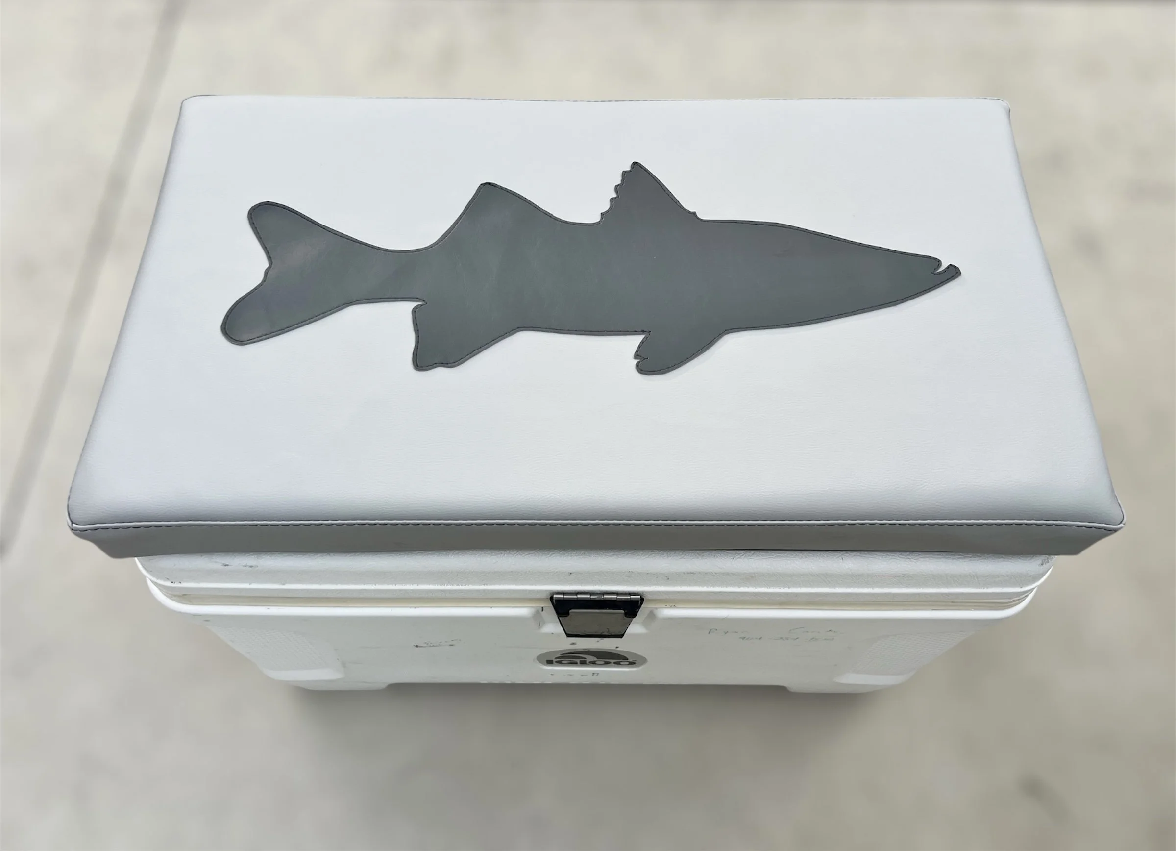 A white cooler with a gray cushioned top, featuring a black fish-shaped decoration on the top surface.