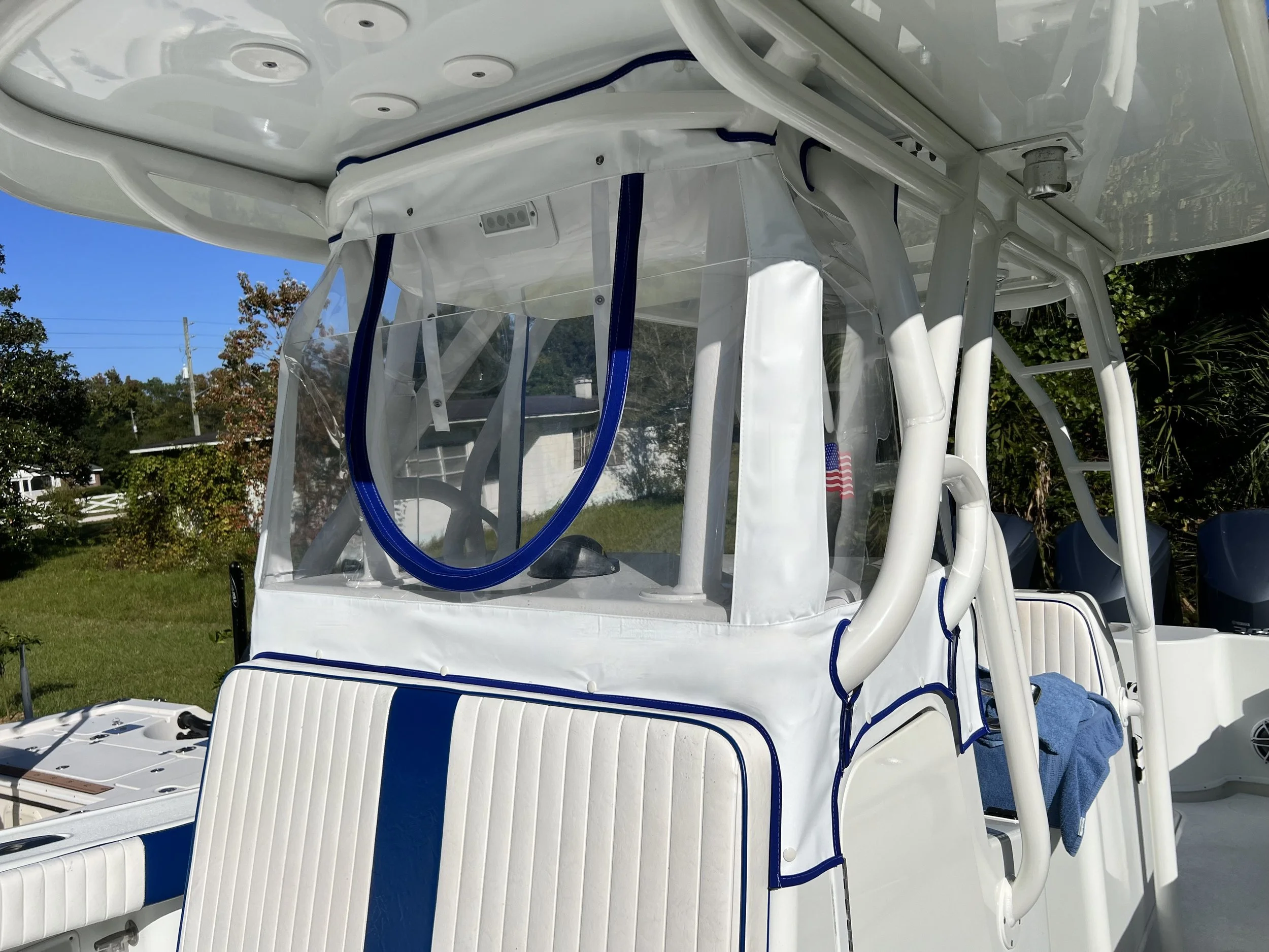 Close-up of a white boat with a transparent windshield, blue accents, and two outboard motors, parked outdoors under a clear blue sky.
